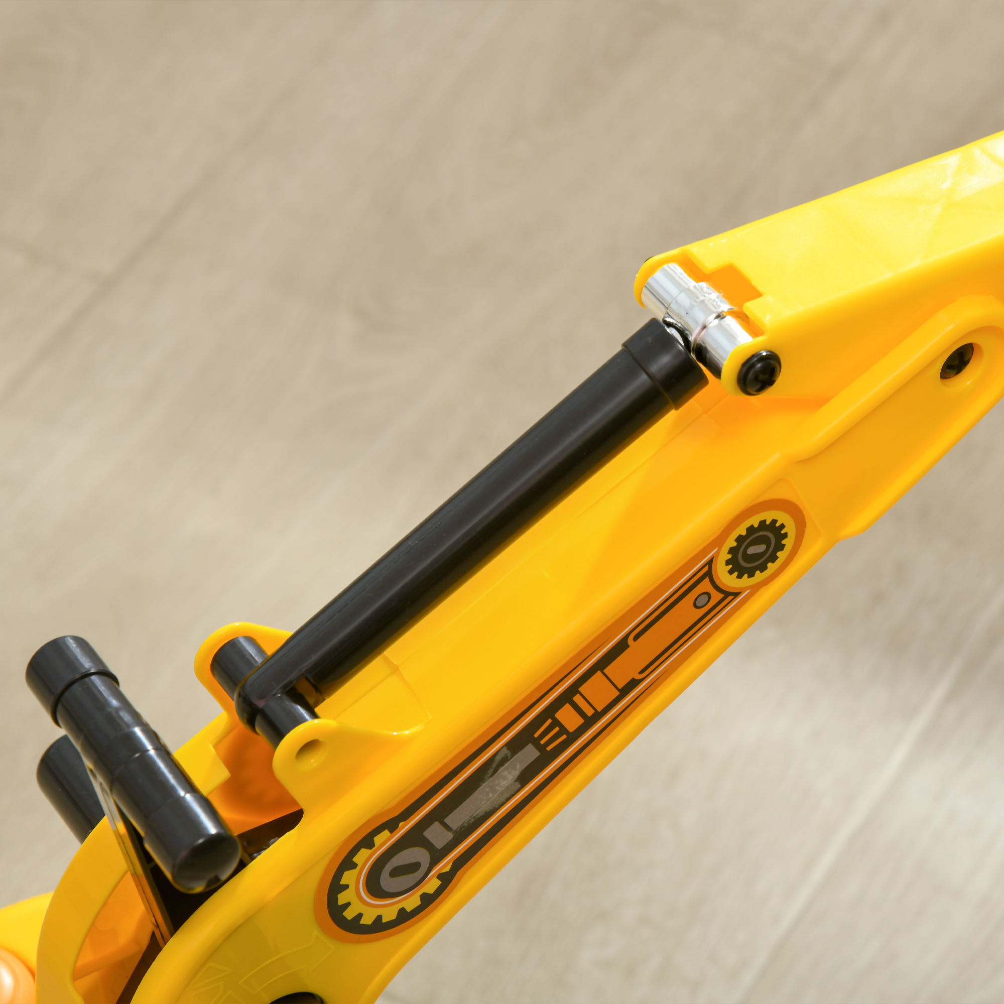 Braccio di escavatore giocattolo giallo con dettagli neri su superficie in legno chiaro.
