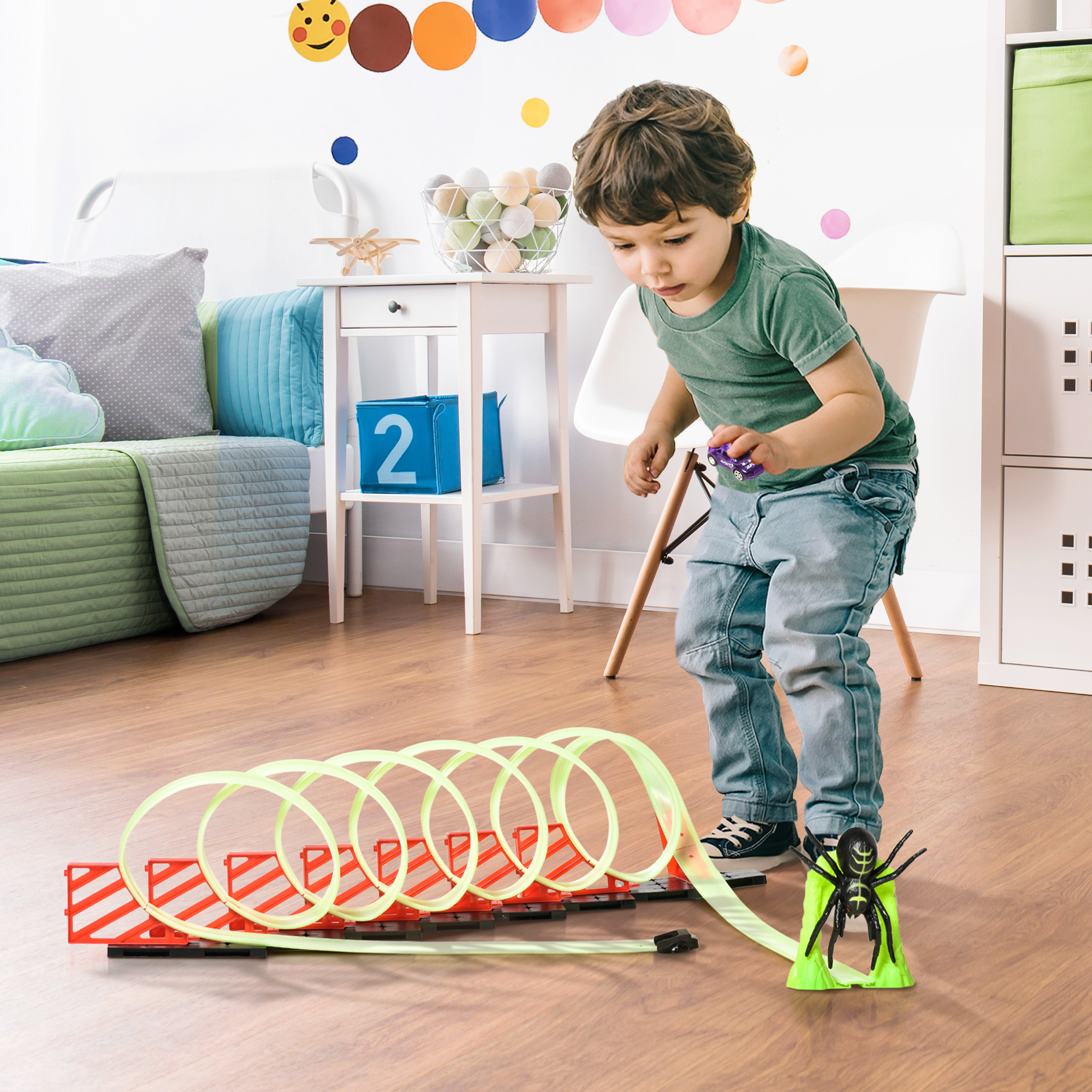 Un bambino gioca con un giocattolo che ha una pista e un ragno sopra. La pista è verde neon.