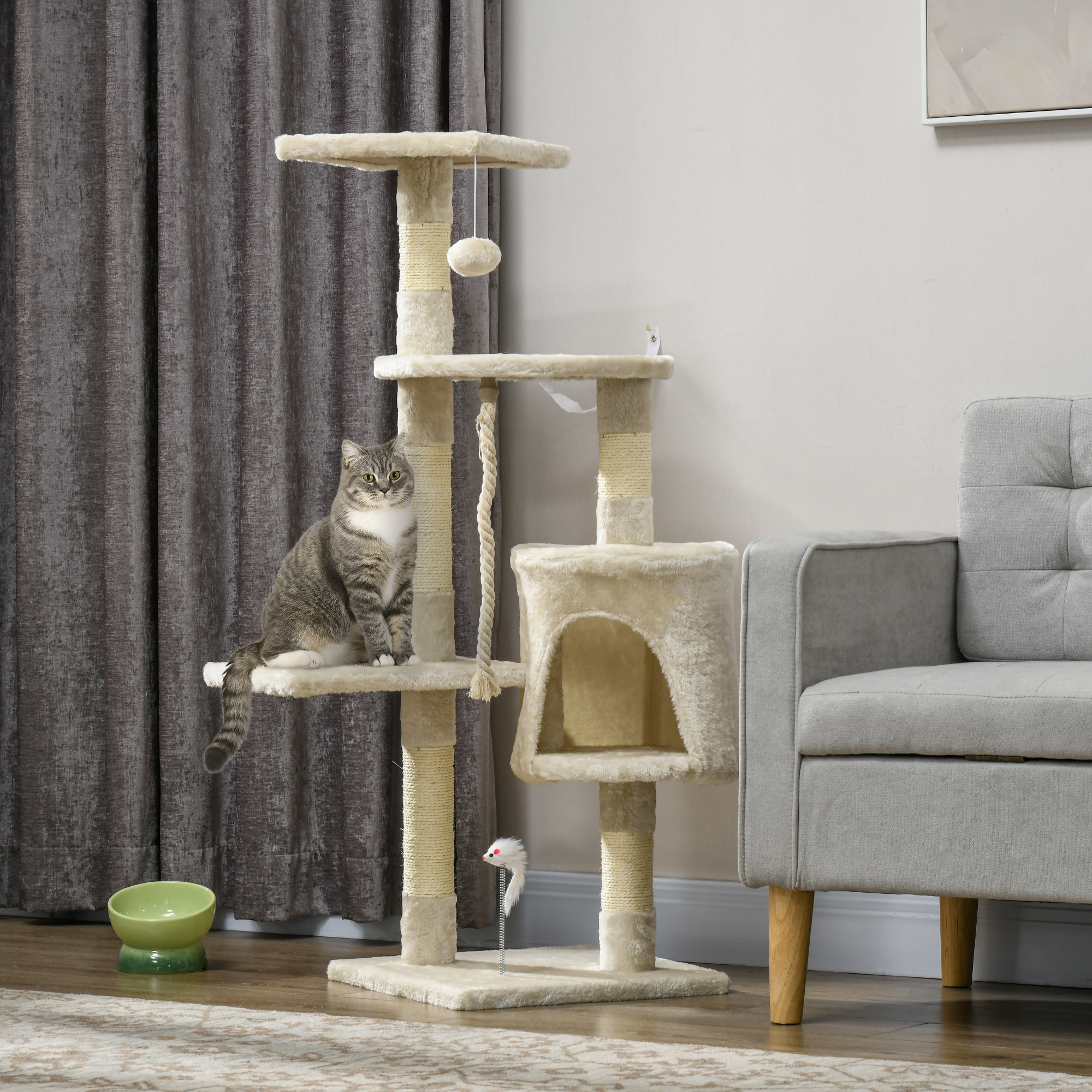 Gato en un árbol para gatos beige. El árbol tiene múltiples niveles, con una bola colgando de arriba.