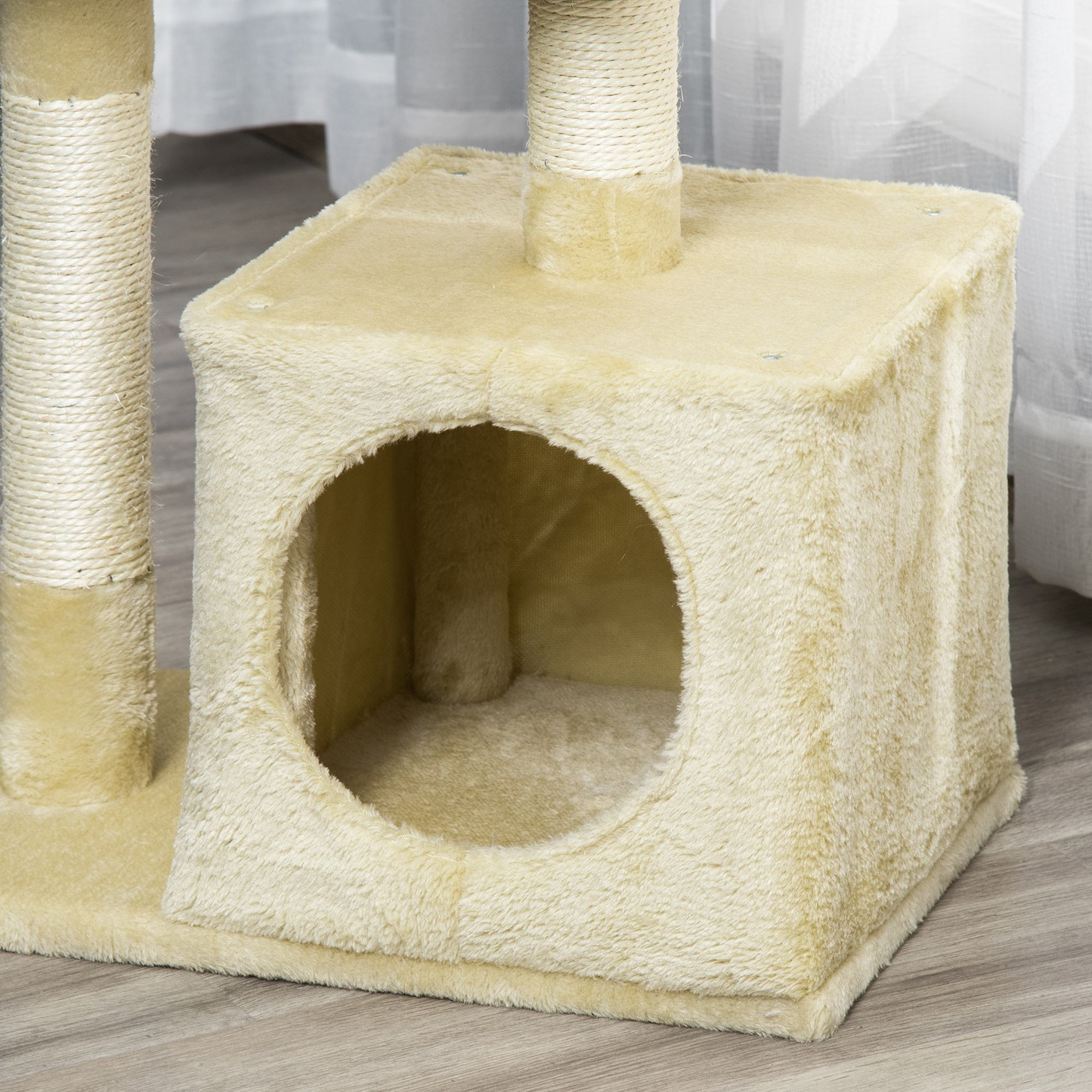 Albero per gatti con cuccia beige, pali per graffiare e apertura rotonda. Sfondo: tenda bianca.