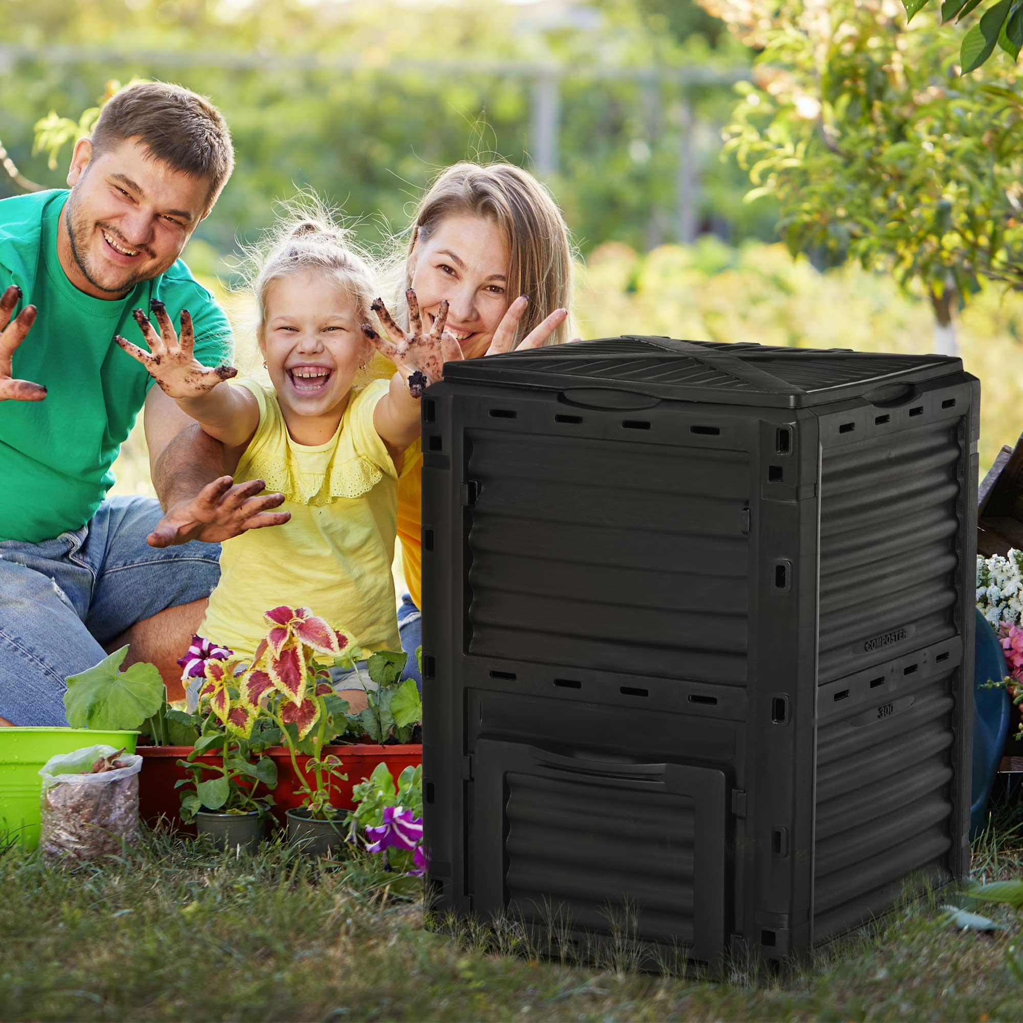 Famiglia vicino a un bidone nero per il compost. Stanno sorridendo e hanno le mani in alto. Fiori vicini.