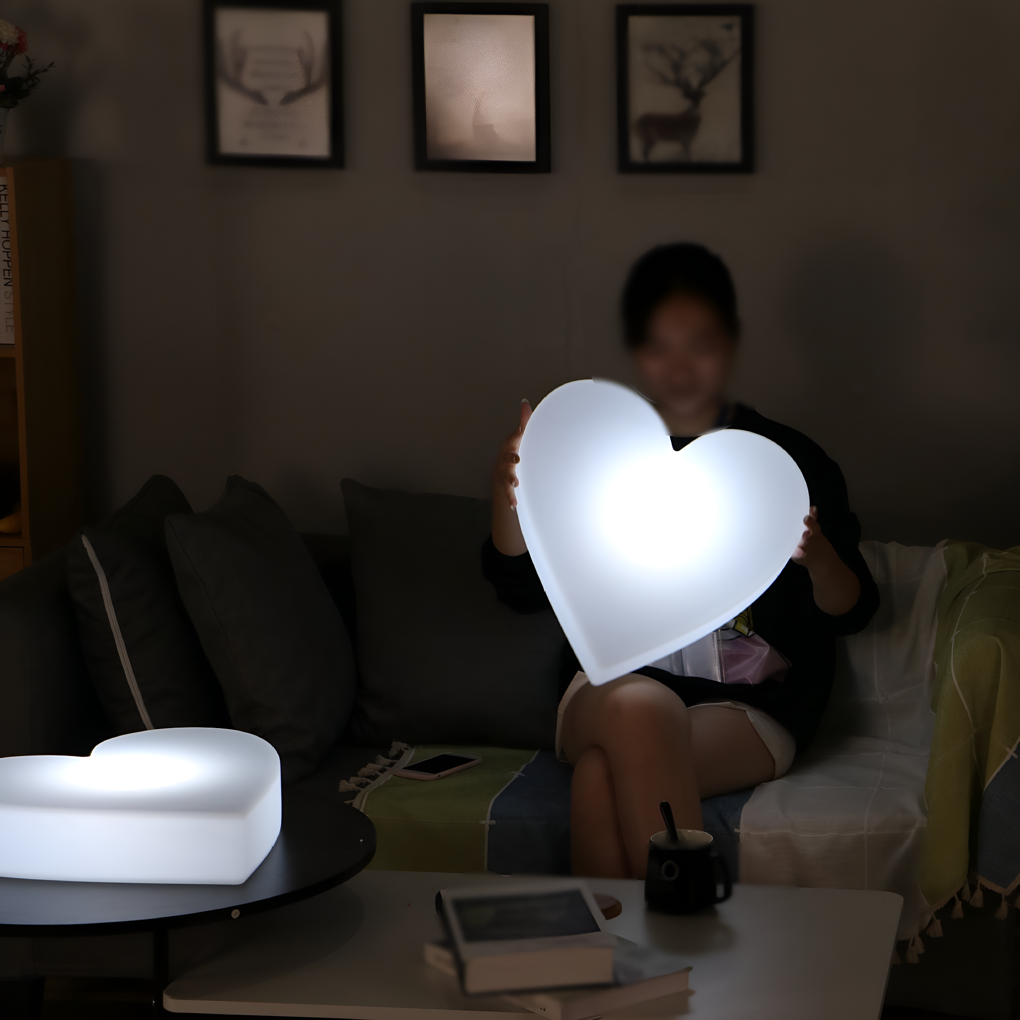 Eine Person hält ein leuchtendes herzförmiges Licht, ein weiteres auf einem Tisch. Dunkles Interieur.