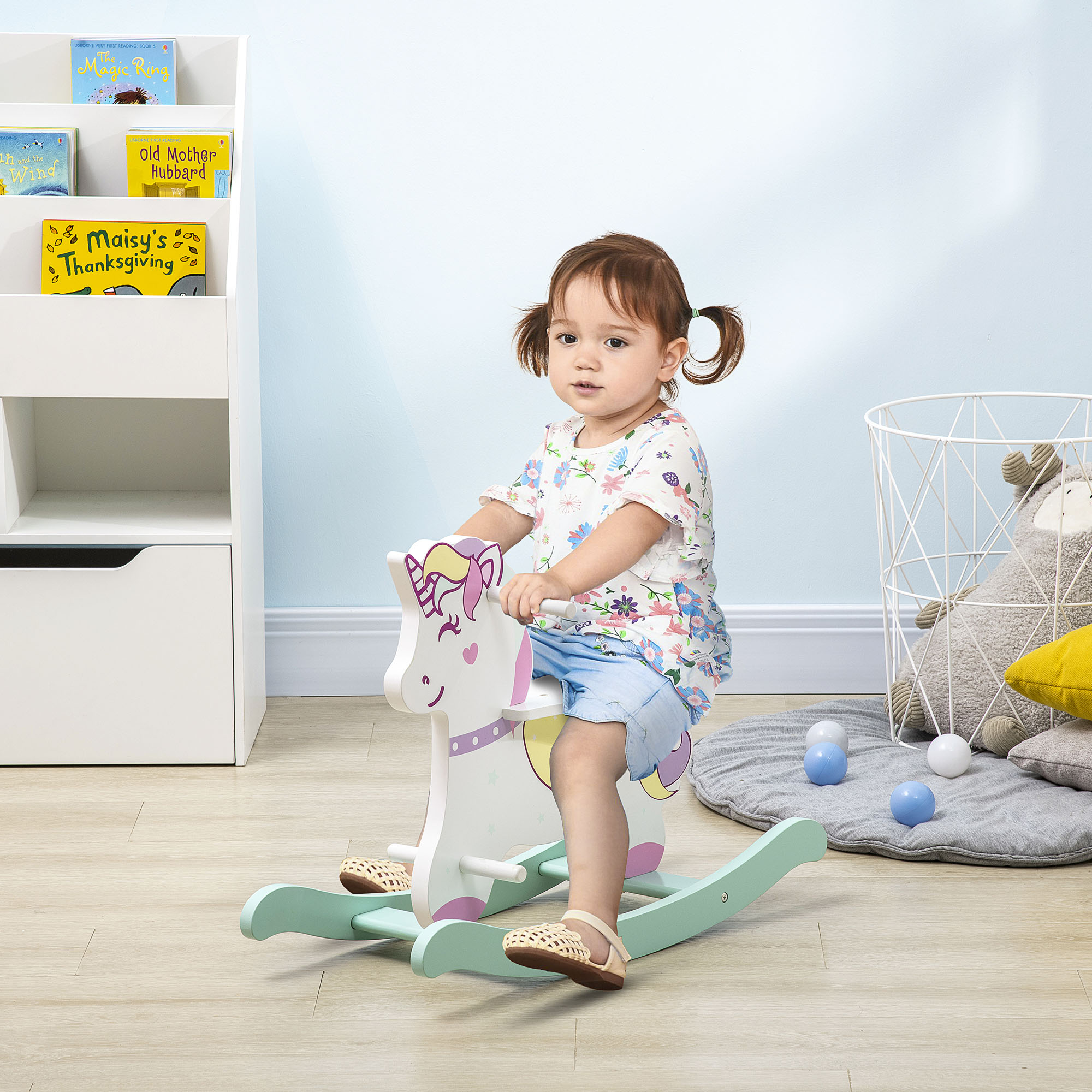 Un bambino piccolo che cavalca un giocattolo a dondolo a forma di unicorno in una stanza con libri e un cestino di filo metallico.