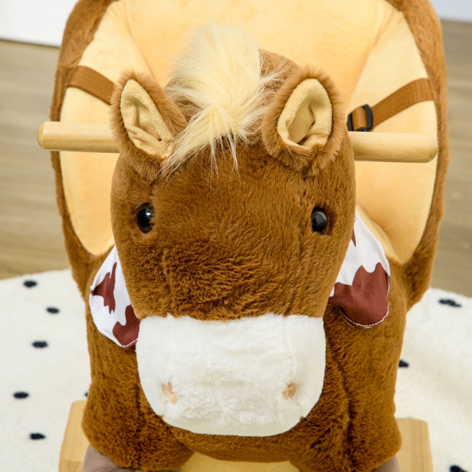 Un giocattolo a dondolo a forma di cavallo marrone con una sciarpa bianca e marrone con stampa di mucca, su un tappeto bianco.