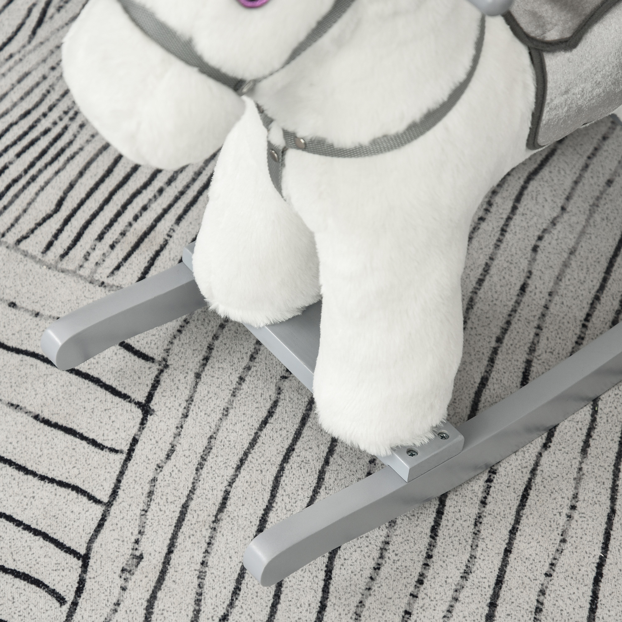Un cavallo a dondolo grigio con corpo bianco e dondoli grigi, ripresa di dettaglio su un tappeto fantasia.