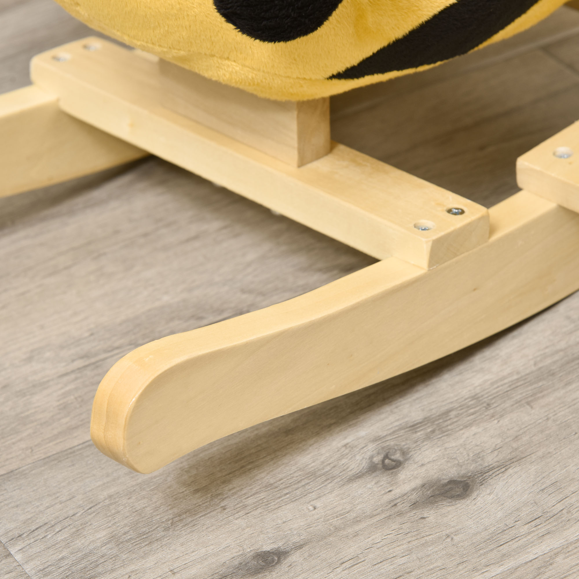 Primo piano di una base a dondolo a forma di ape gialla e nera, struttura in legno su pavimento grigio.