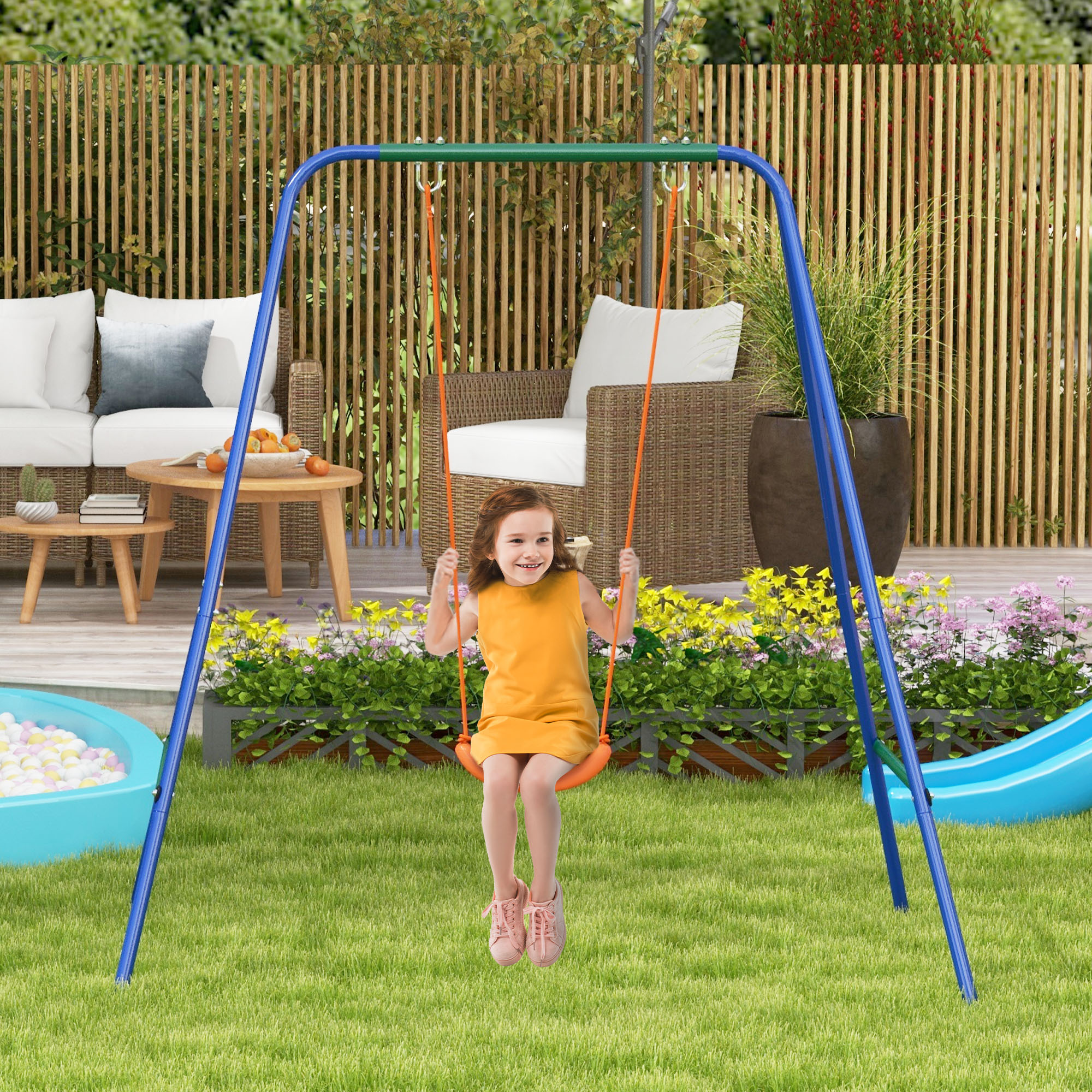 Una niña con un vestido naranja se balancea en un columpio azul y verde en un césped.