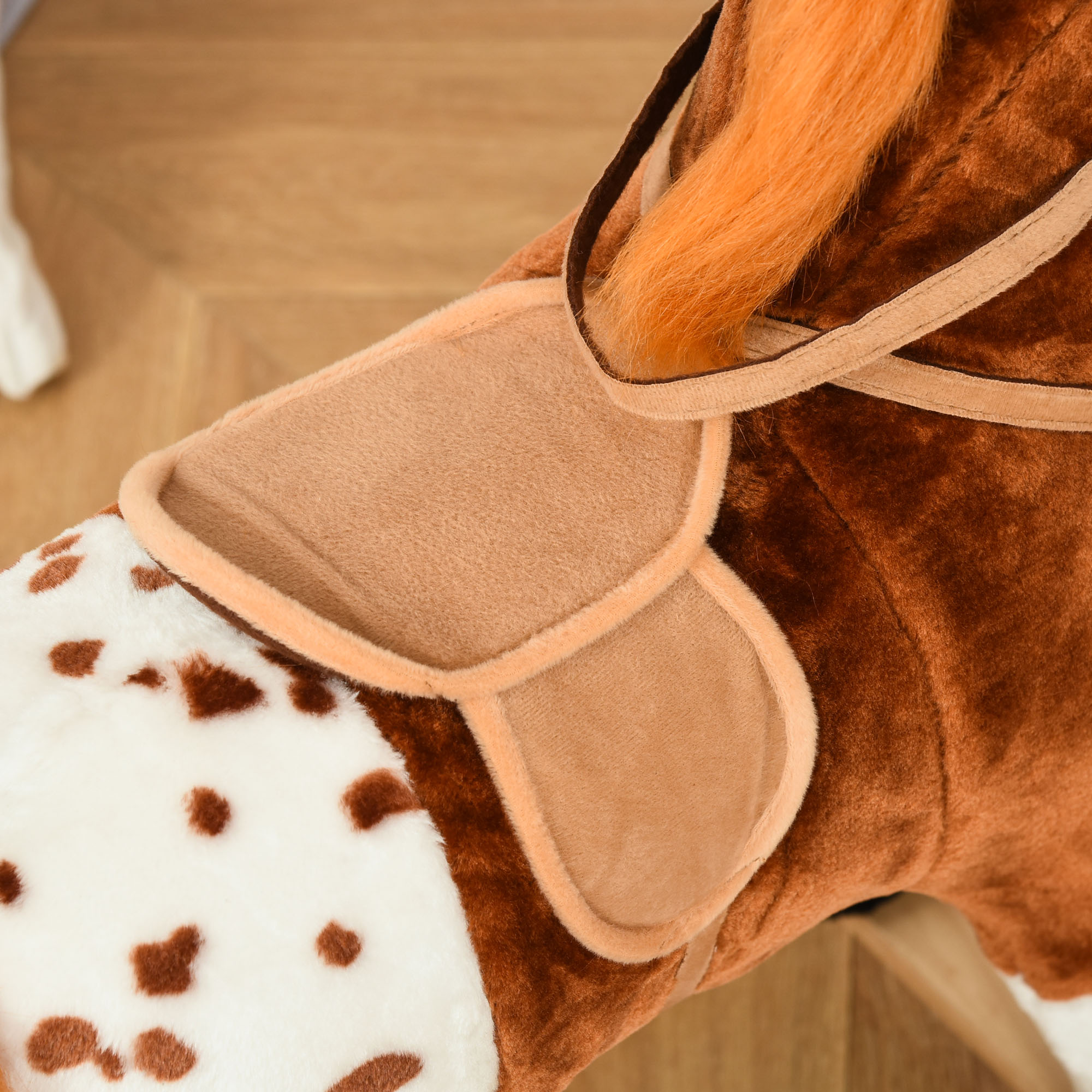 Un cavallo a dondolo marrone e bianco con sella. Criniera arancione. Primo piano.