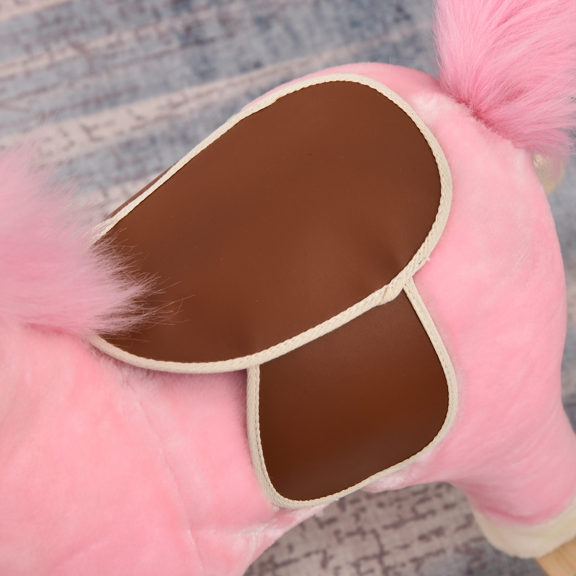 Un sedile di cavallo a dondolo rosa con pannelli laterali in similpelle marrone e pelliccia rosa.