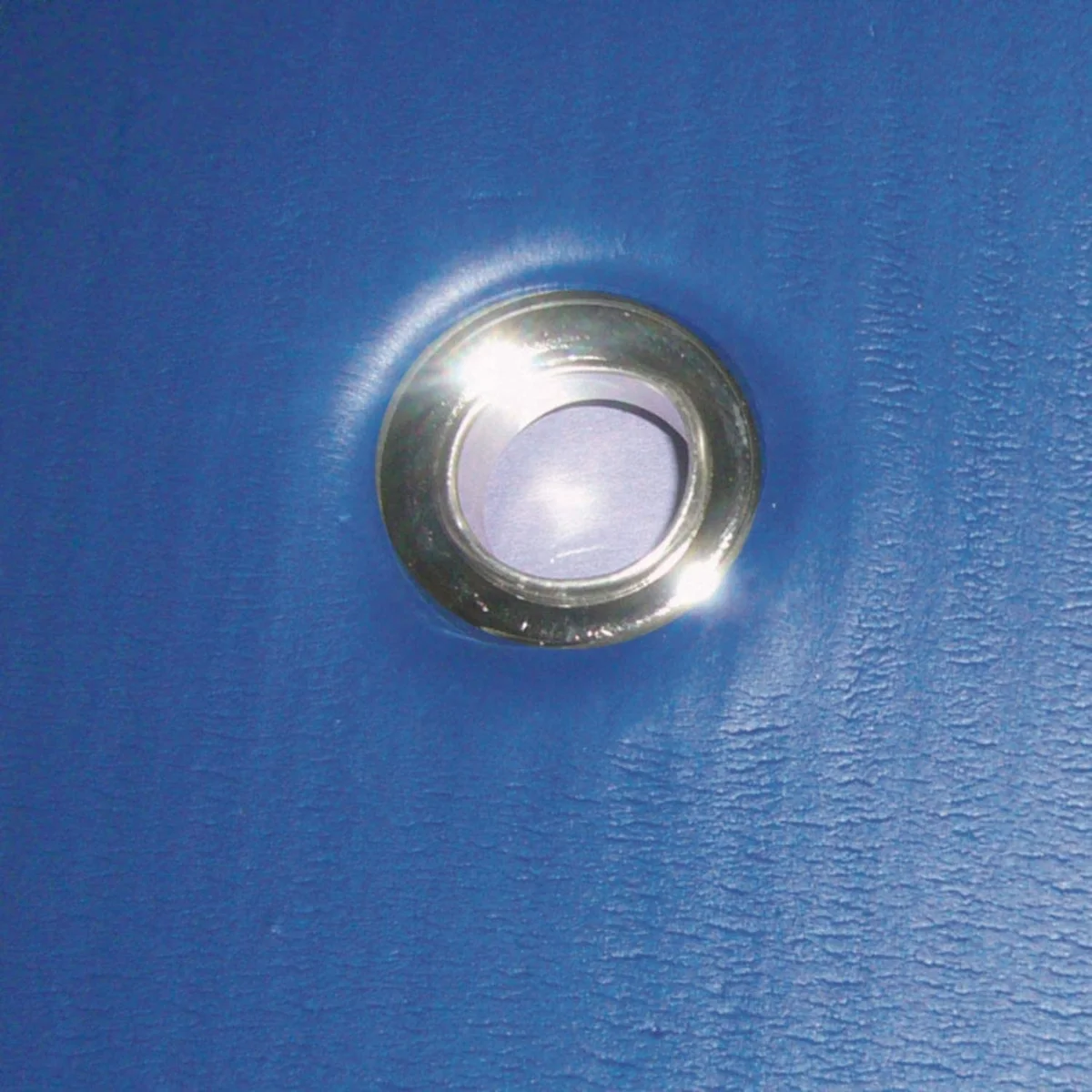Close-up of a blue surface with a circular, silver-rimmed eyelet. Shiny surface.