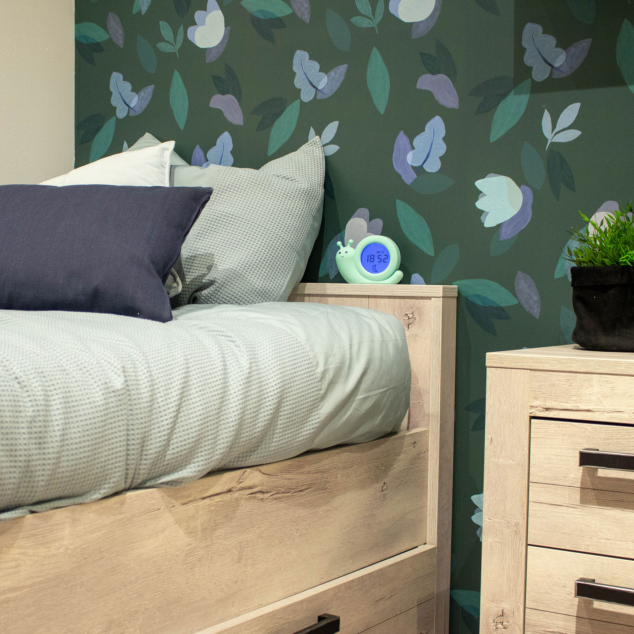 Une chambre avec un lit, une table de chevet et un mur à motifs floraux. Une horloge numérique est sur la table de chevet.