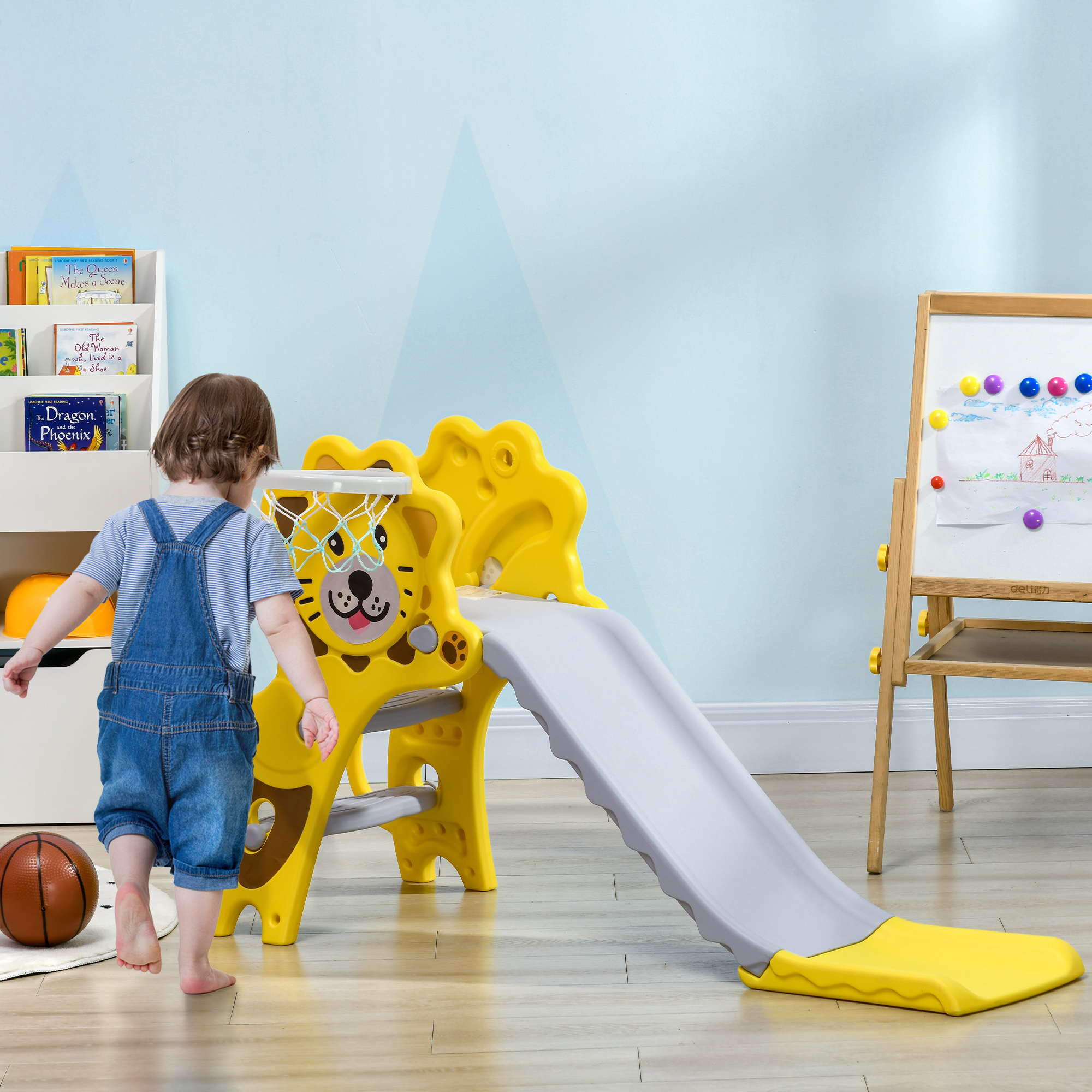 Un bambino gioca su uno scivolo a forma di leone giallo. Un pallone da basket sul pavimento, una libreria dietro.