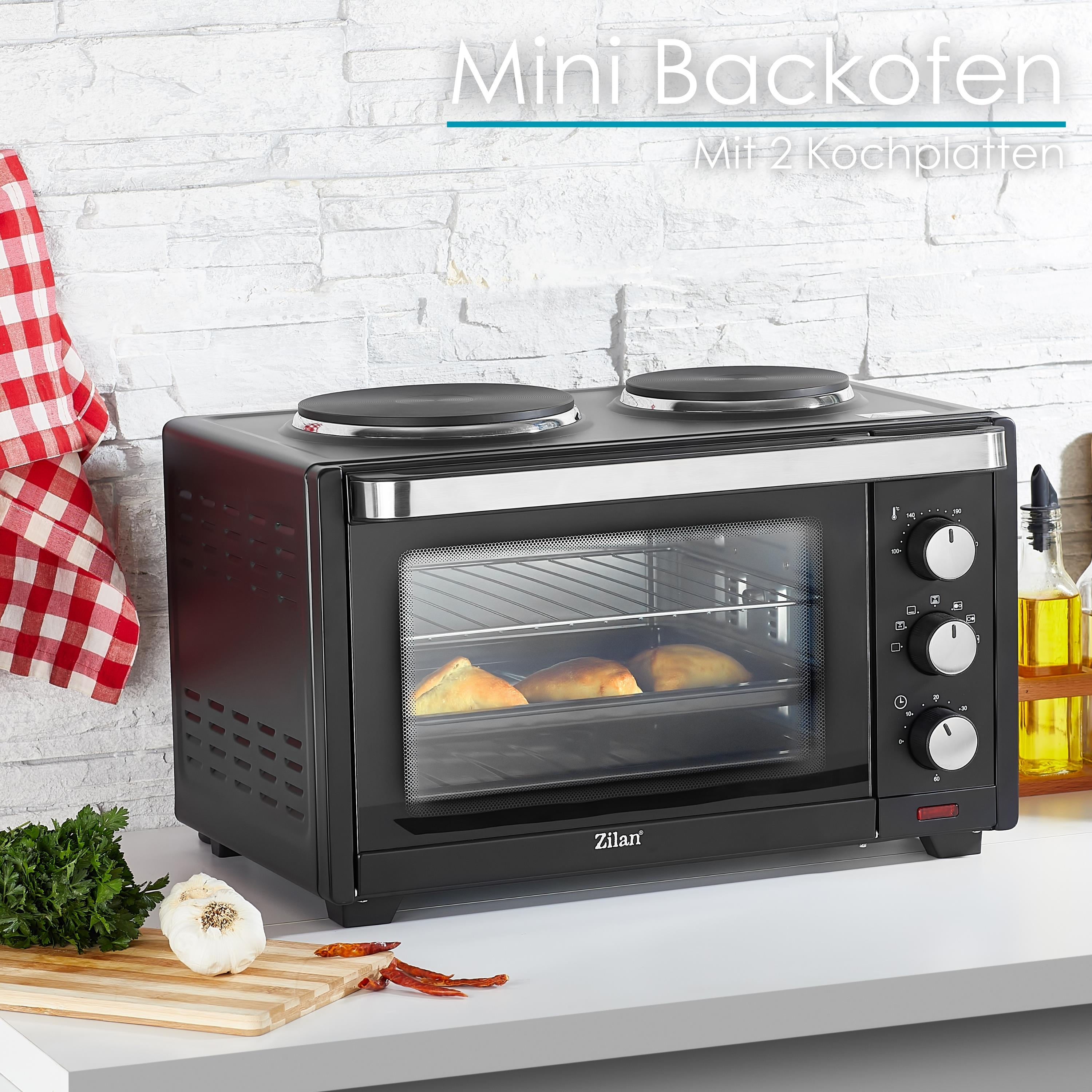 Mini-Backofen schwarz mit zwei Kochfeldern oben, mit Essen drin, auf weißer Oberfläche.