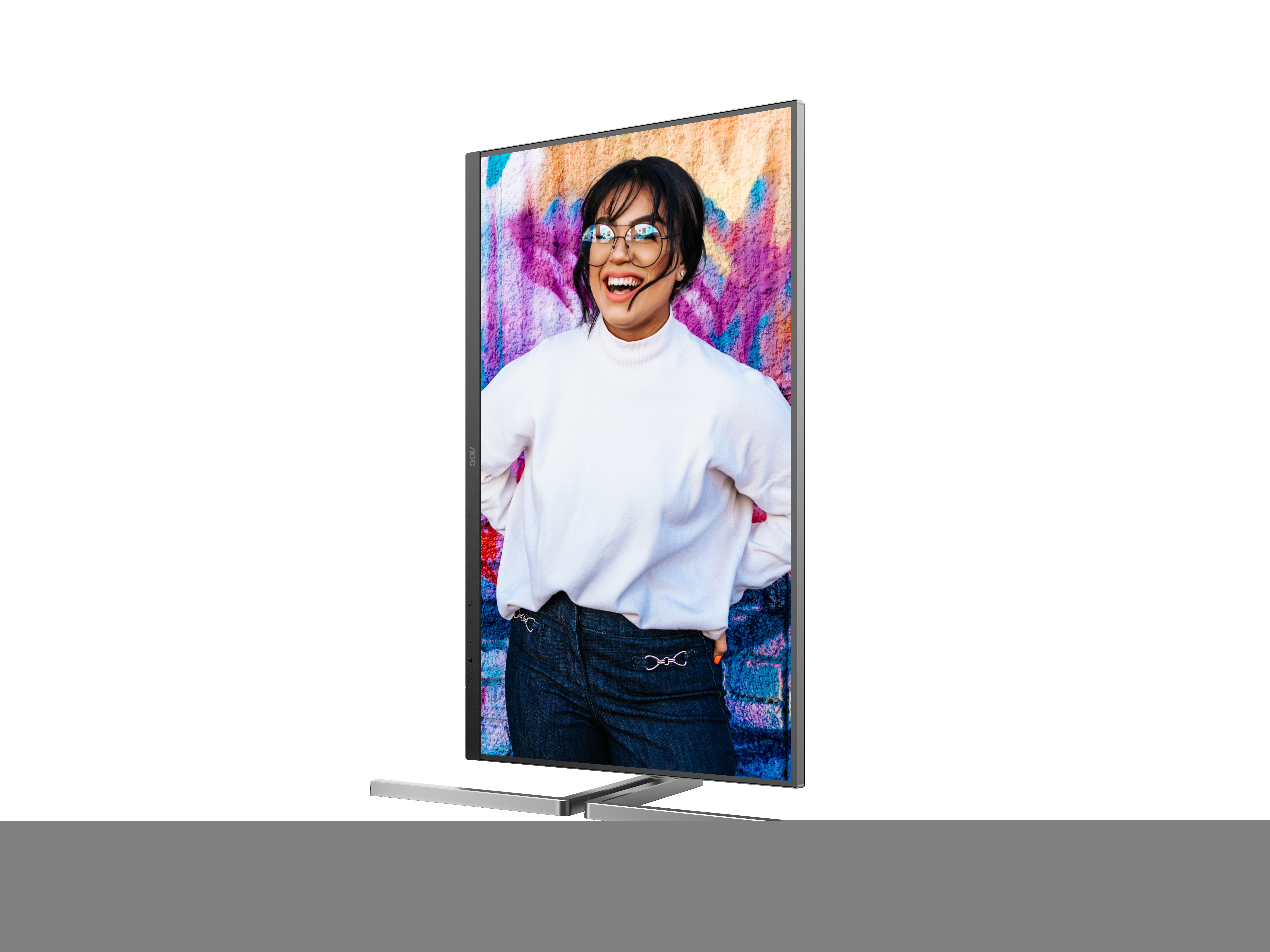 Kobieta w białym swetrze i okularach stoi przed monitorem, który wyświetla ścianę pokrytą graffiti.