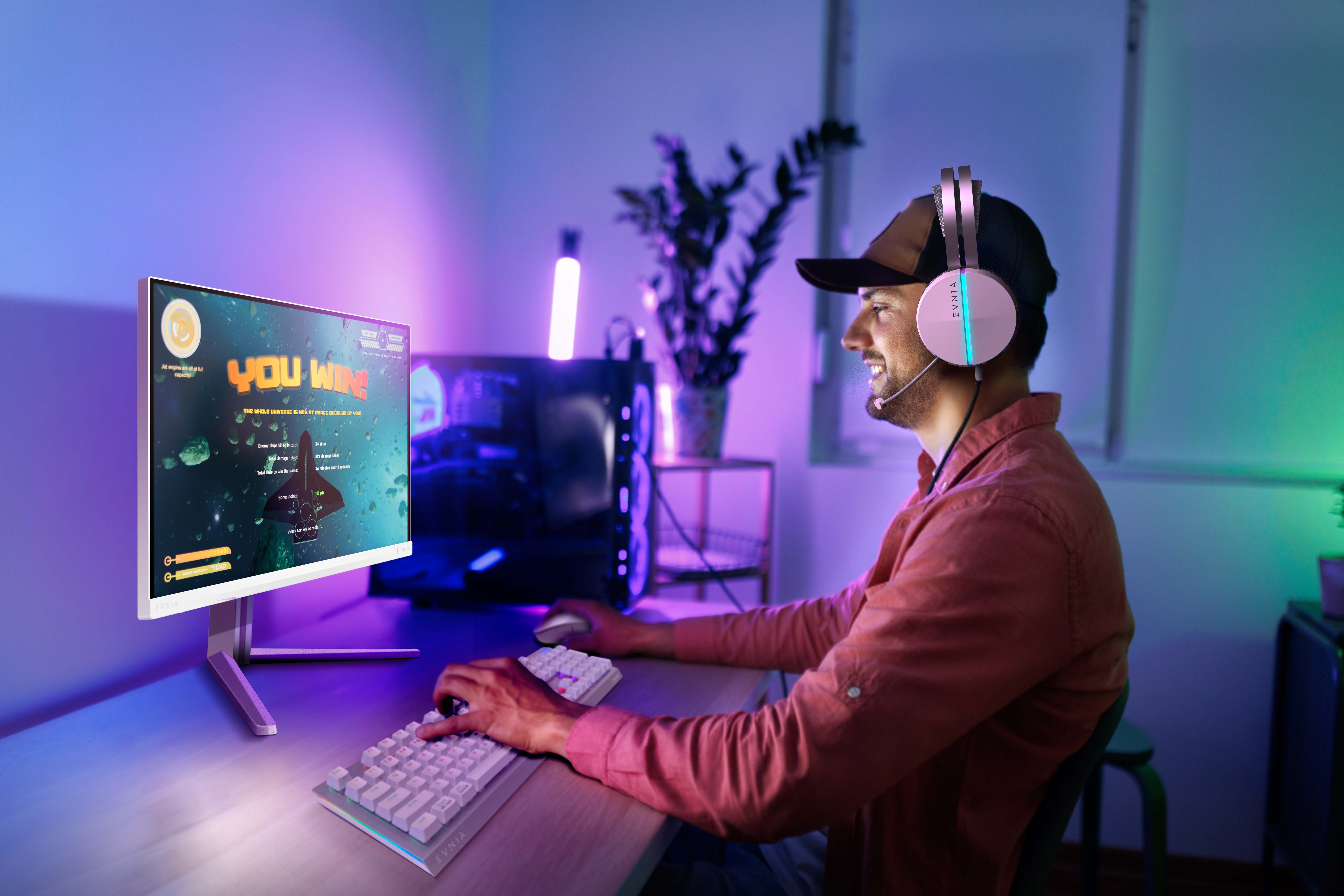 Gracz w słuchawkach i czapce gra w grę na monitorze, oświetlonym na niebiesko i fioletowo.