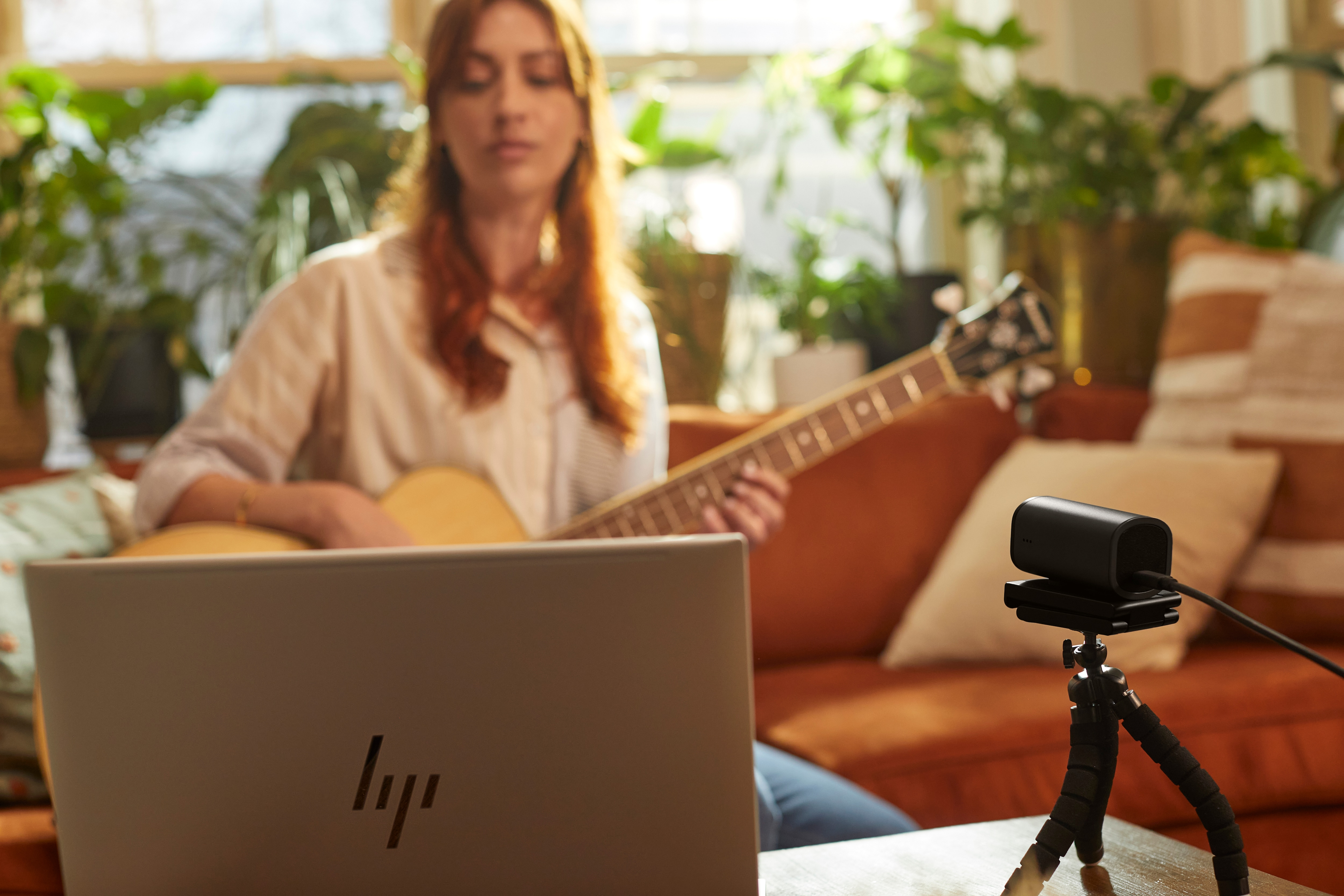 Kobieta grająca na gitarze przed laptopem z kamerą internetową na statywie.