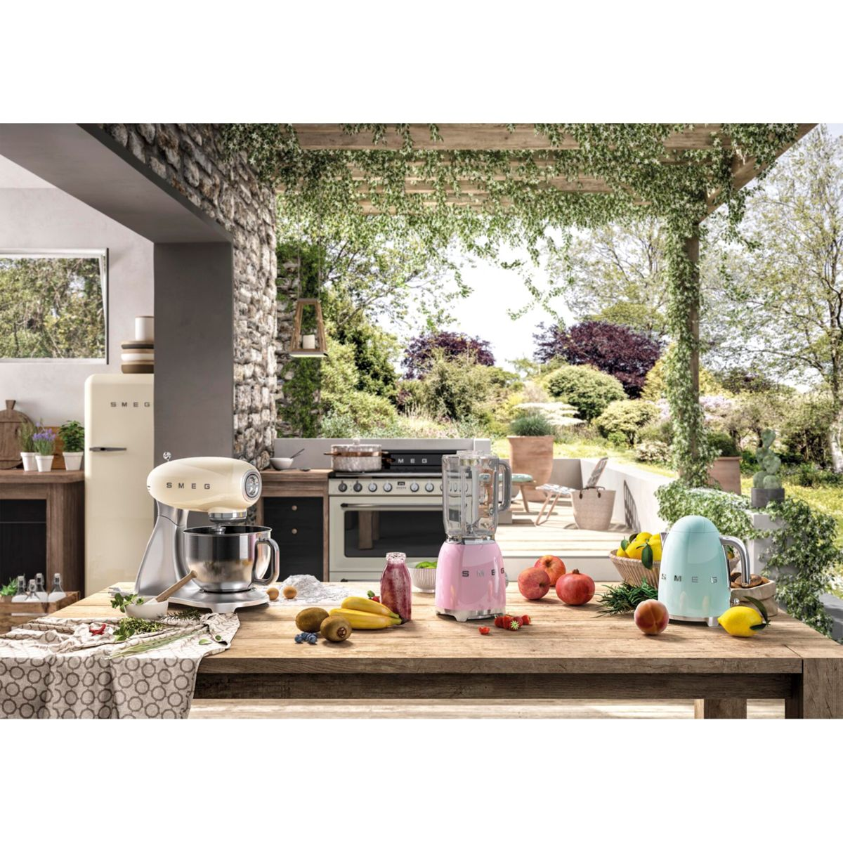Scena kuchenna ze stołem, mikserem, blenderem, lodówką i różnymi owocami. Tłem jest ogród.
