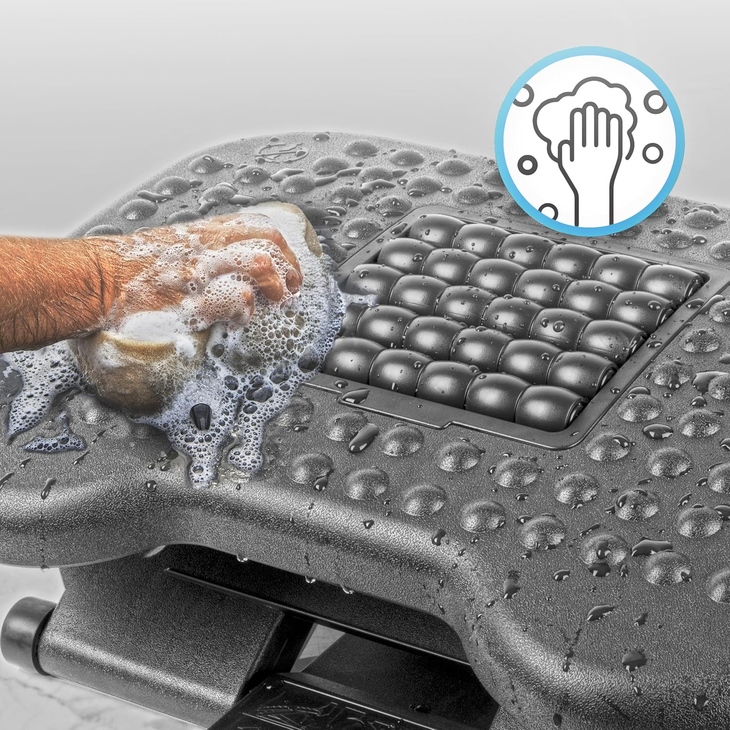 Una mano limpia un reposapiés negro con una esponja y agua jabonosa. Un icono de lavado de manos en el fondo.