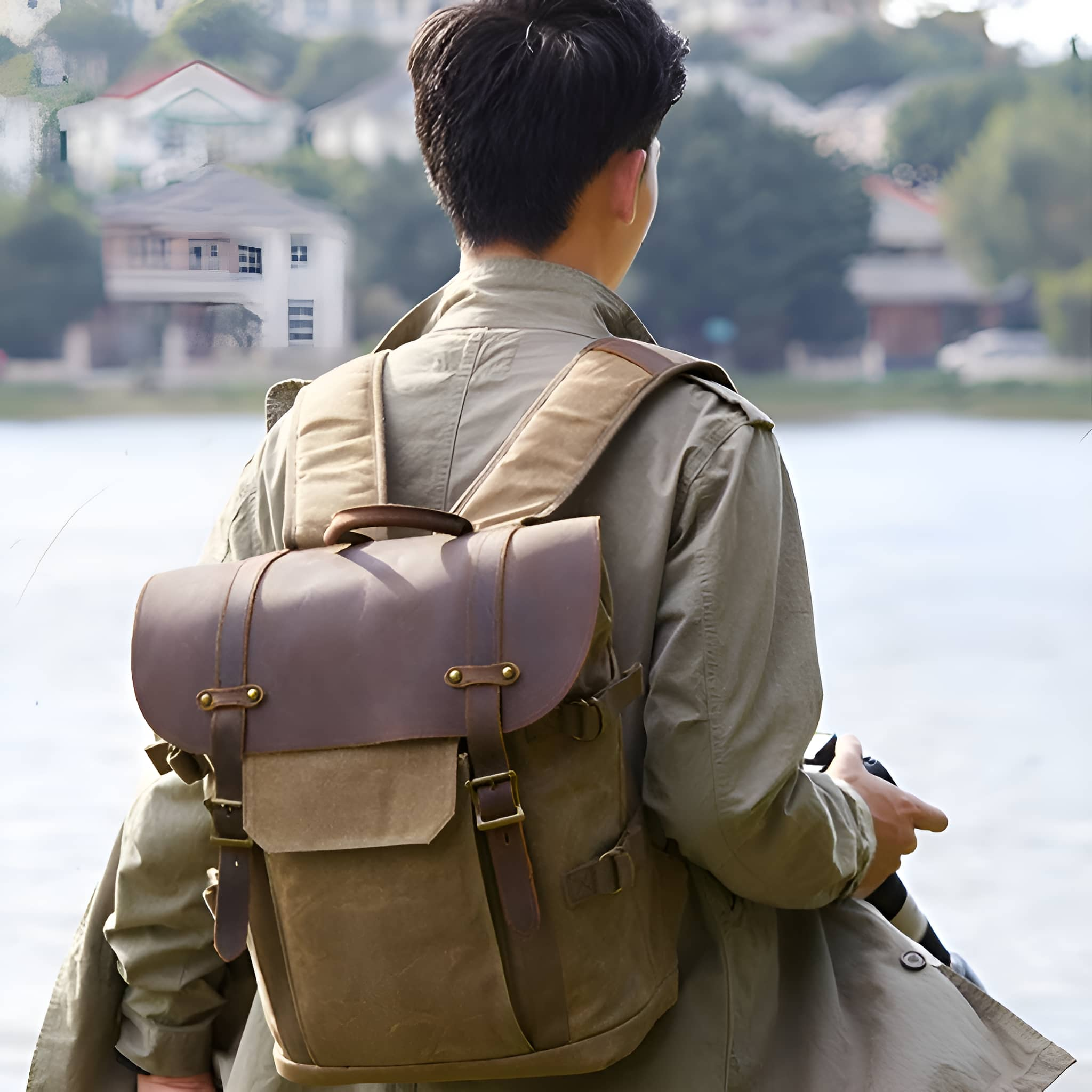 Mann mit Rucksack am Wasser. Häuser und Bäume im Hintergrund.