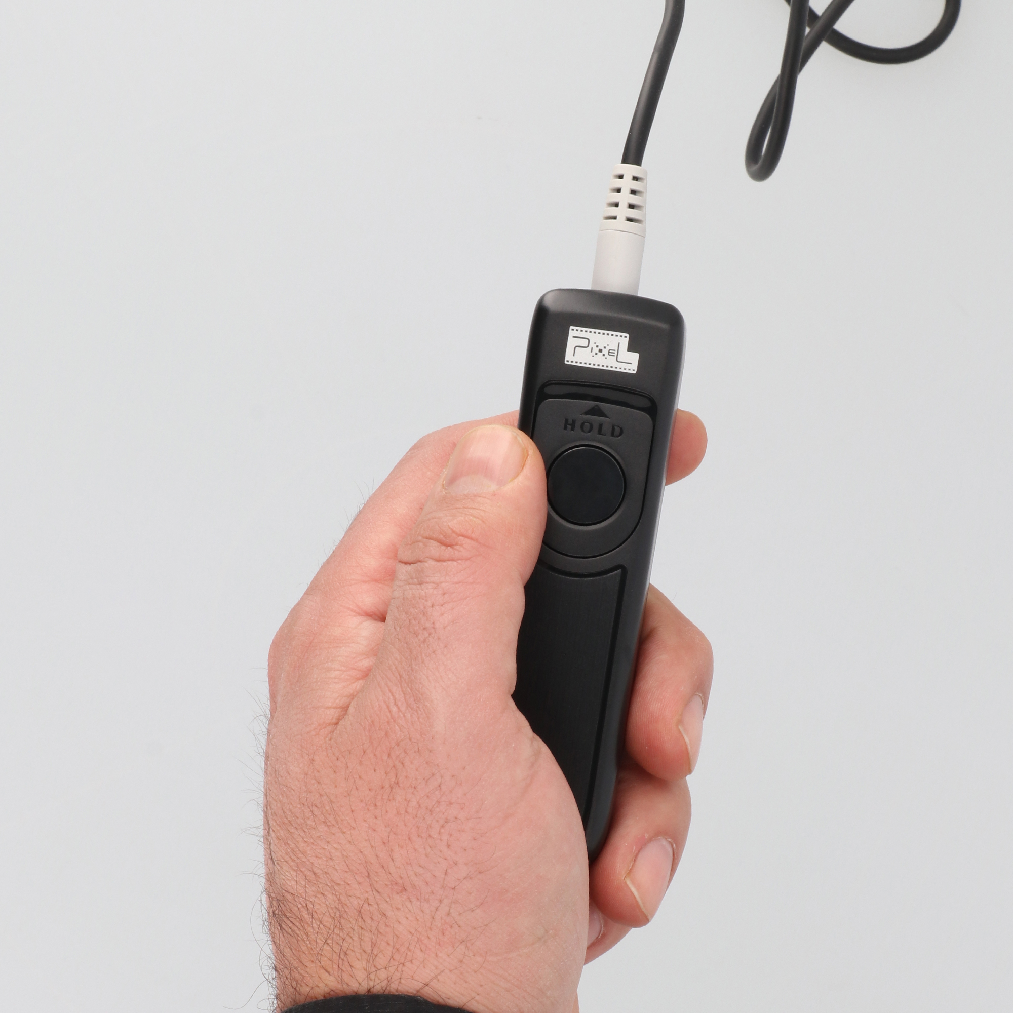 Hand hält eine schwarze Fernbedienung mit weißem Kabel. Weißer Hintergrund.
