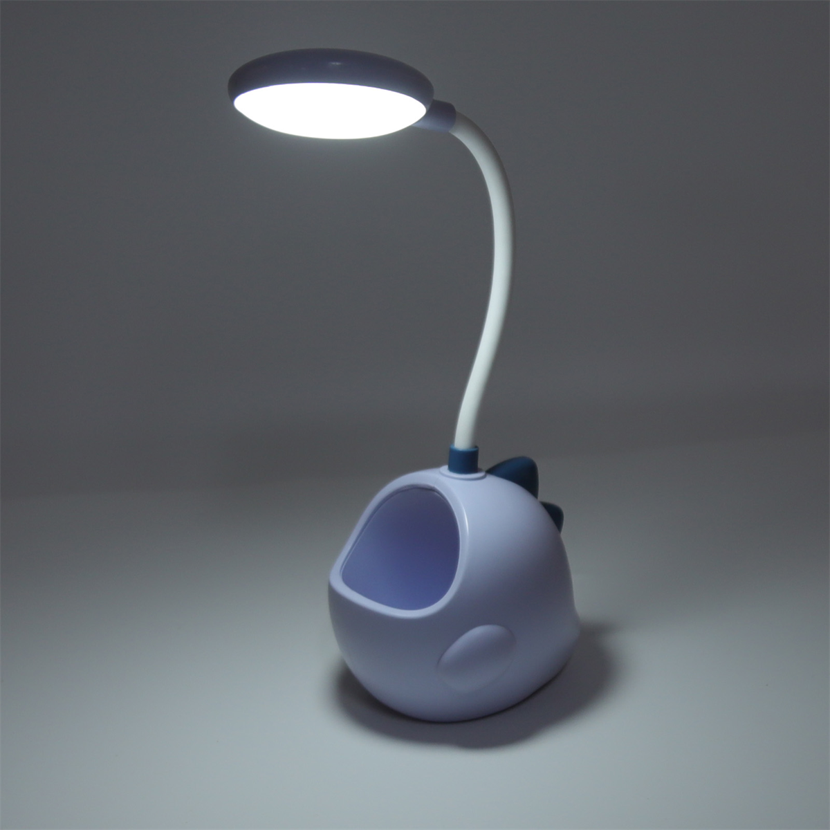 Eine blaue, dinosaurierförmige Schreibtischlampe mit weißem Licht oben. Der Sockel ist ein Stifthalter.