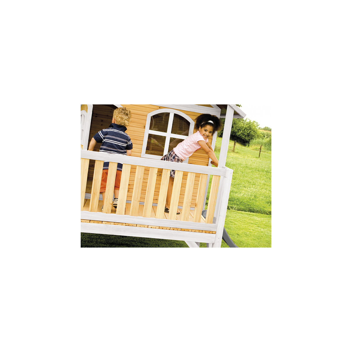 Zwei Kinder spielen auf einem Holzspielhaus mit Veranda. Ein Kind schaut in die Kamera.