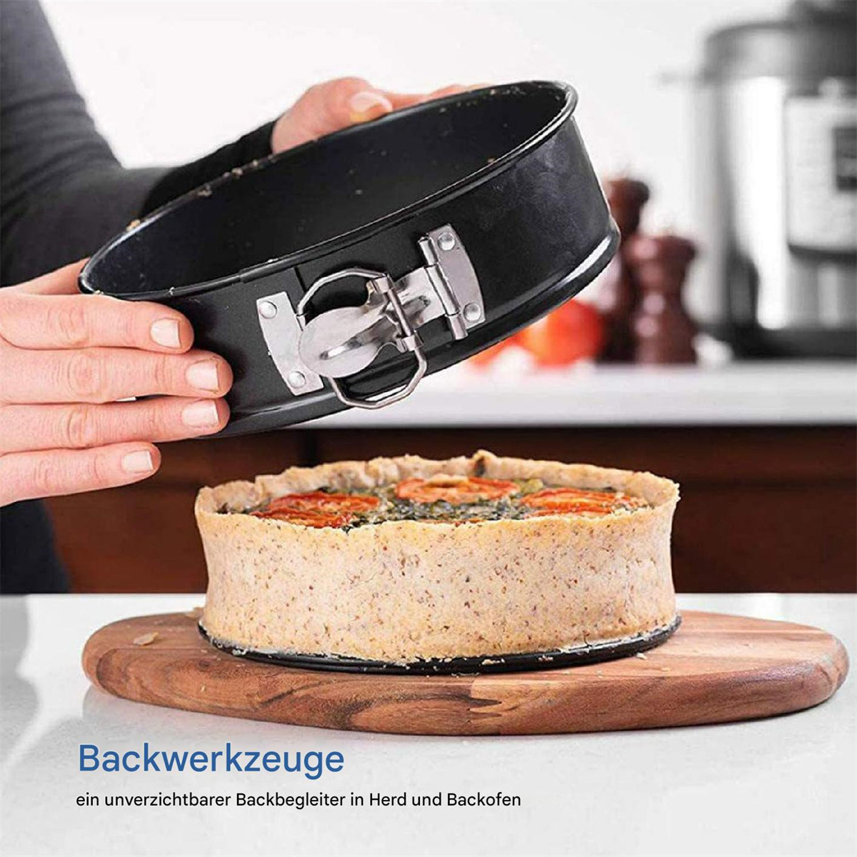 Eine schwarze Springform mit einem gebackenen Kuchen auf einem Holzbrett, der Hintergrund ist eine Küche.
