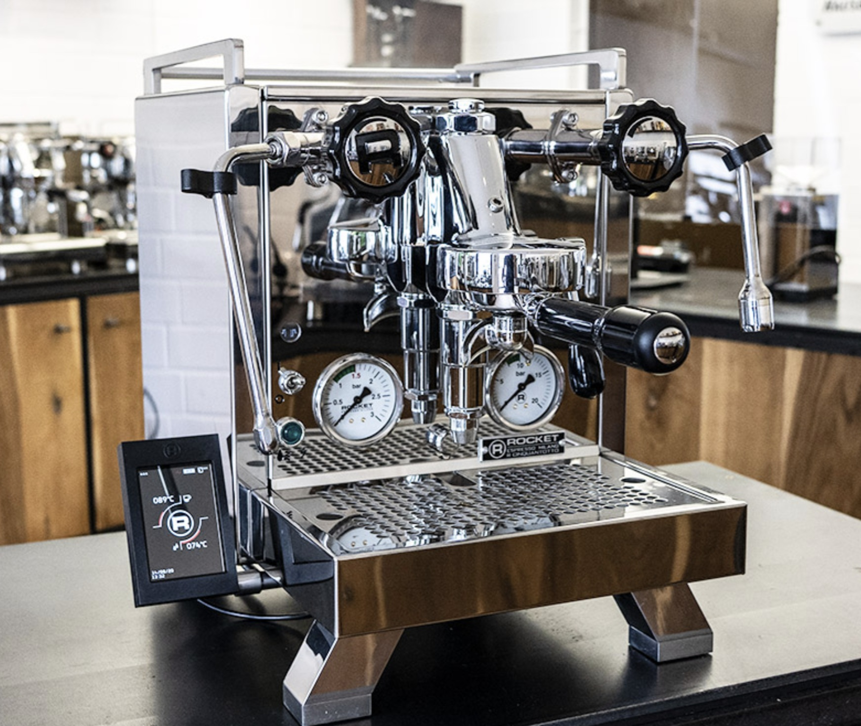Macchina per espresso cromata con manometri e display digitale. Maniglie nere e superficie metallica.