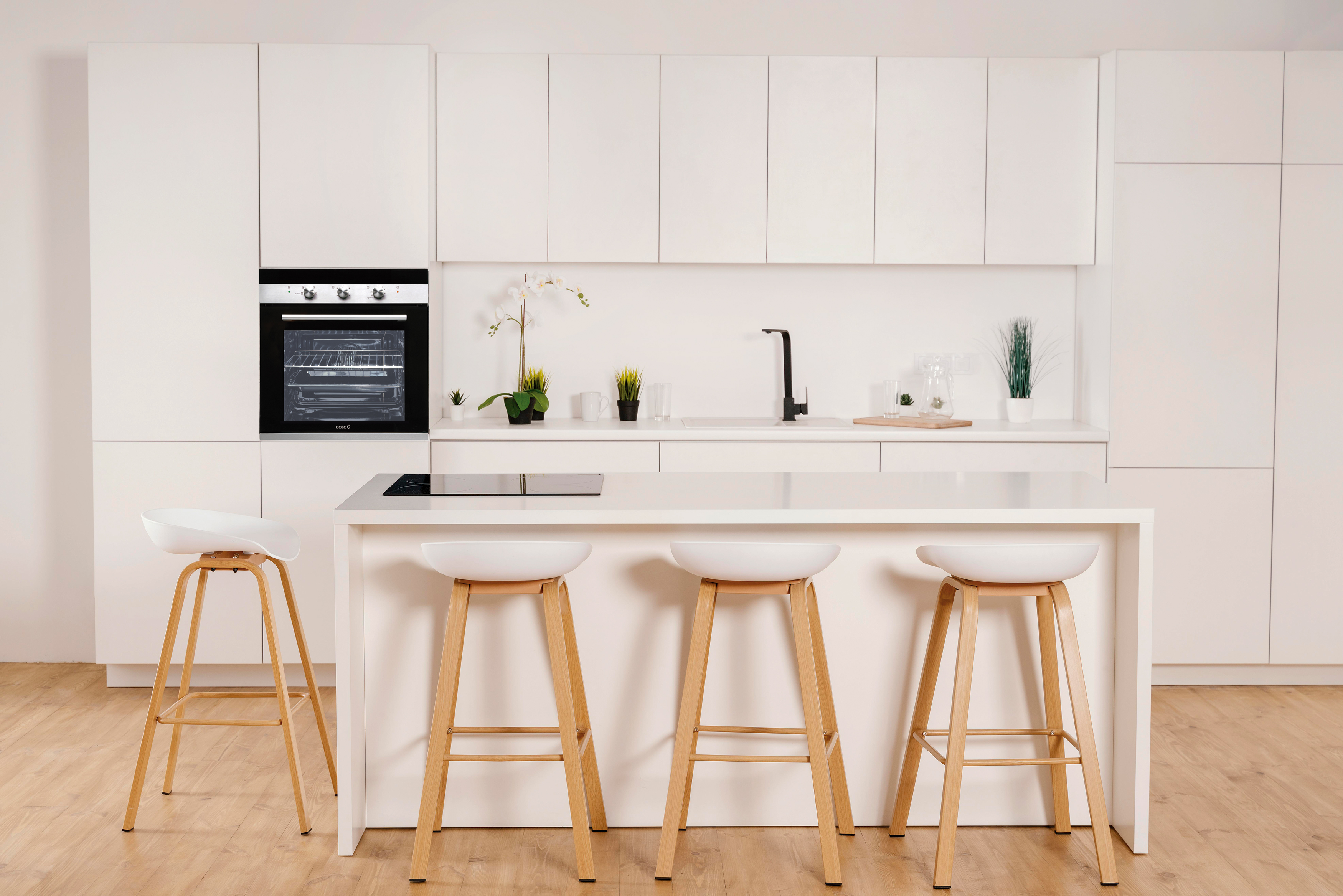 Cocina blanca moderna con isla, tres taburetes, horno y armarios superiores. Diseño minimalista.