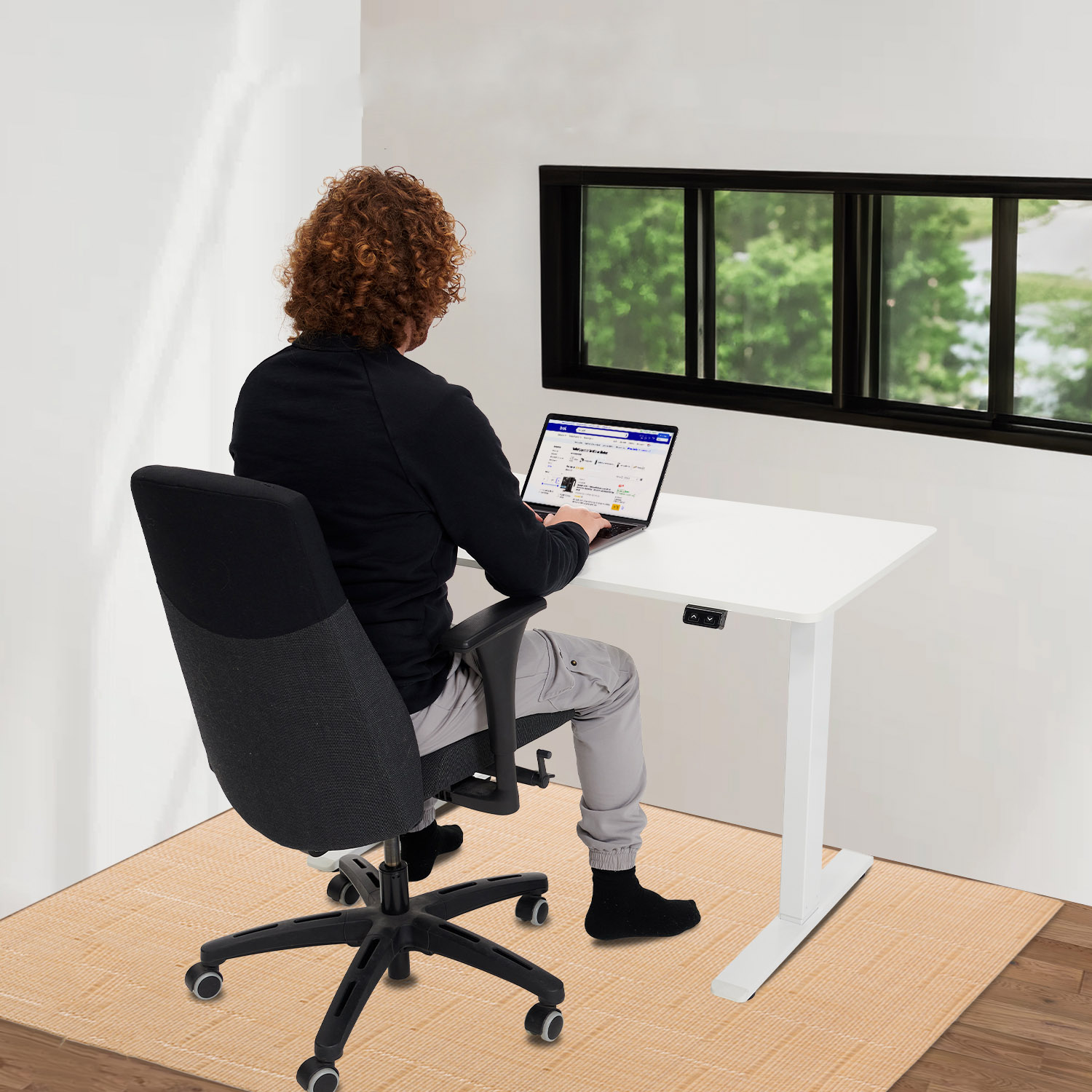 Persoon die op een laptop werkt aan een staande bureau, bij een raam.
