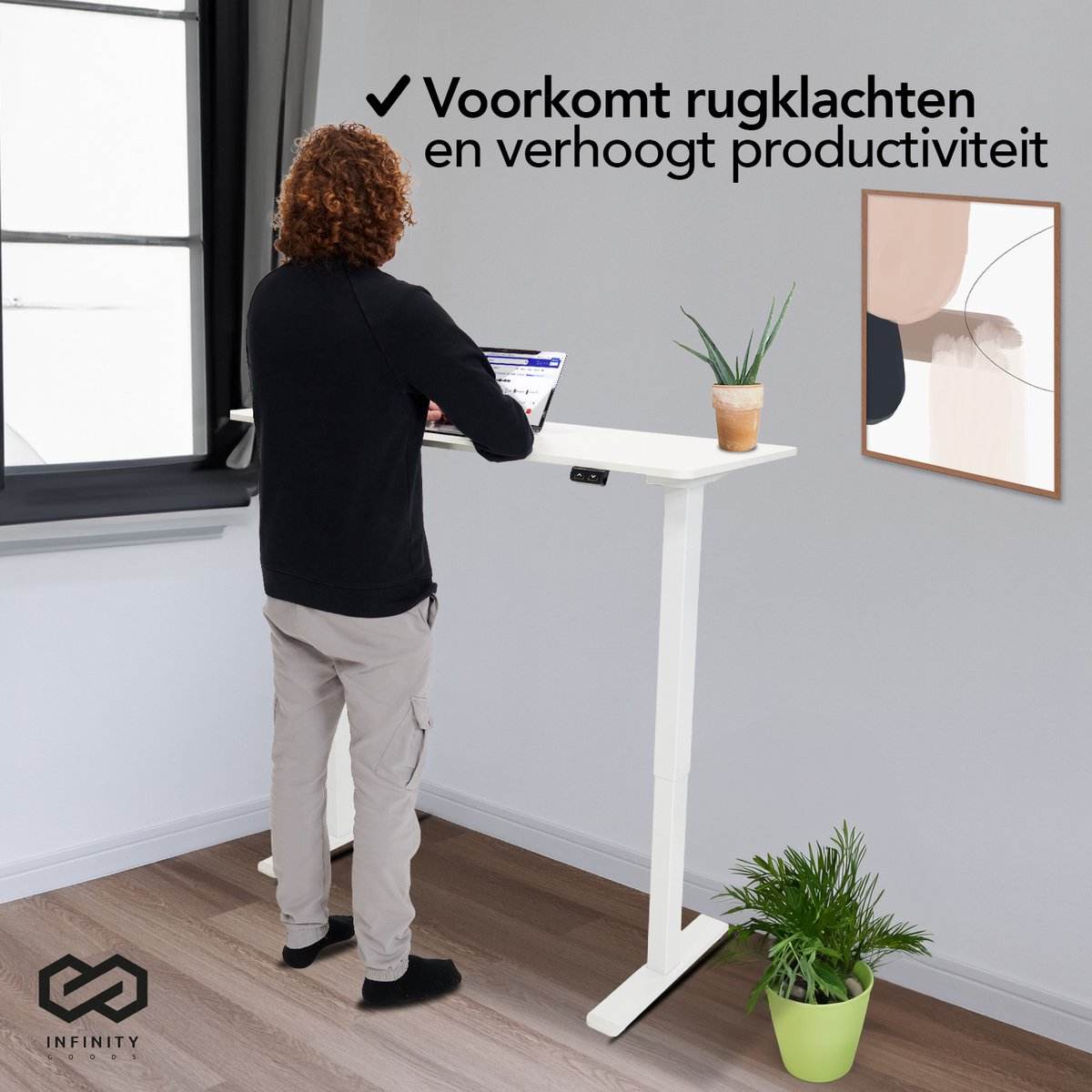 Een man die aan een witte staande bureau met een laptop staat, bij een raam en een schilderij.