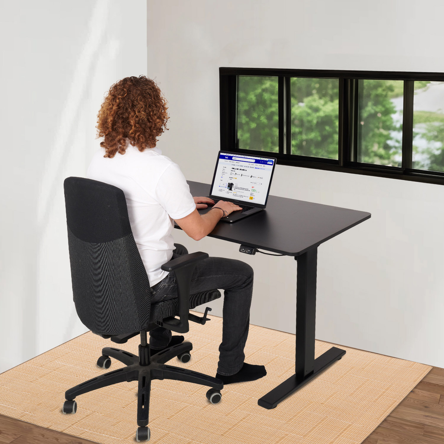 Een persoon die op een laptop werkt aan een zwart bureau in een goed verlichte kamer.