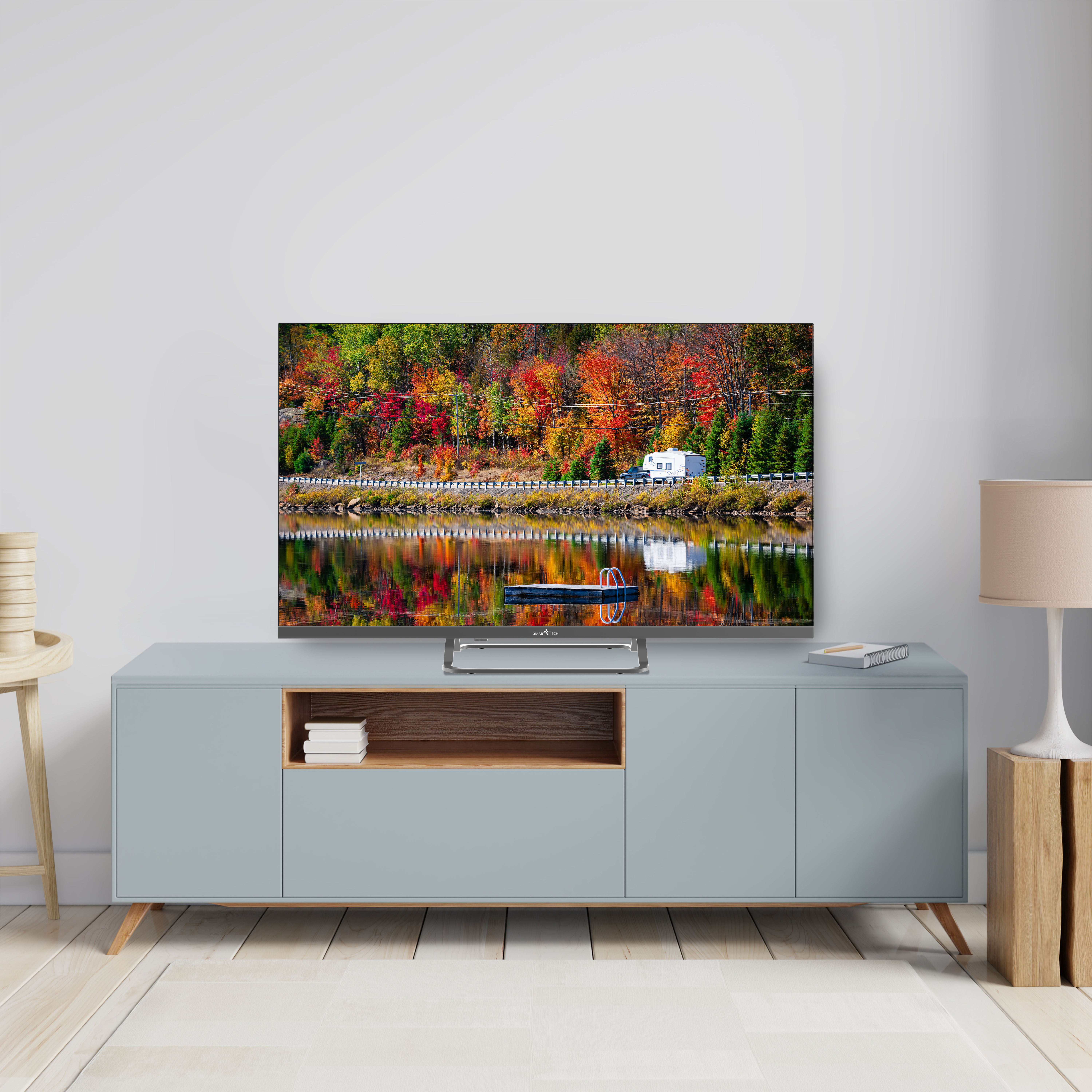 Un televisore con una scena autunnale colorata su un mobile blu. Lampada e sgabello vicini.