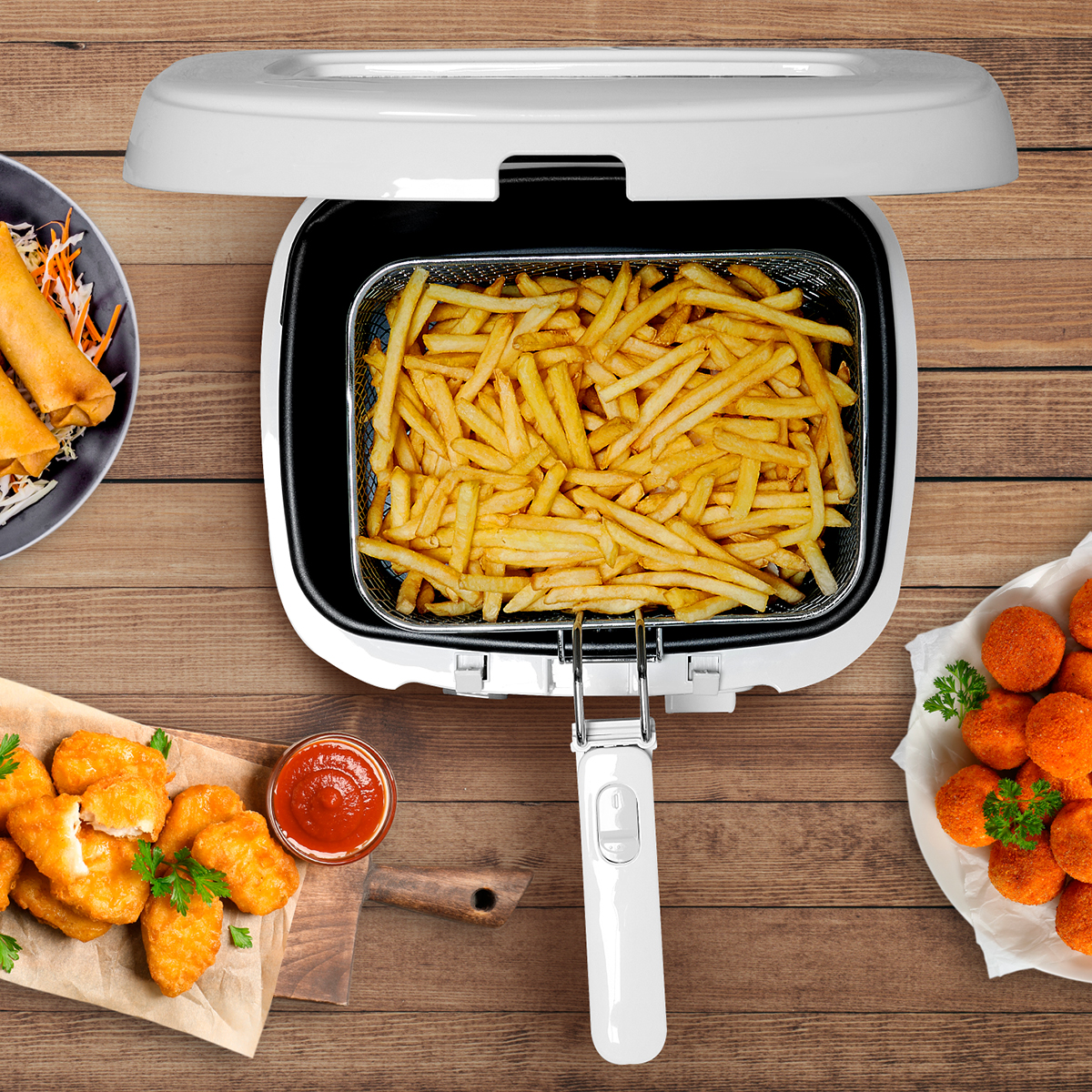 Eine offene Fritteuse mit Pommes, Frühlingsrollen, Nuggets und Fleischbällchen auf einem Holztisch.