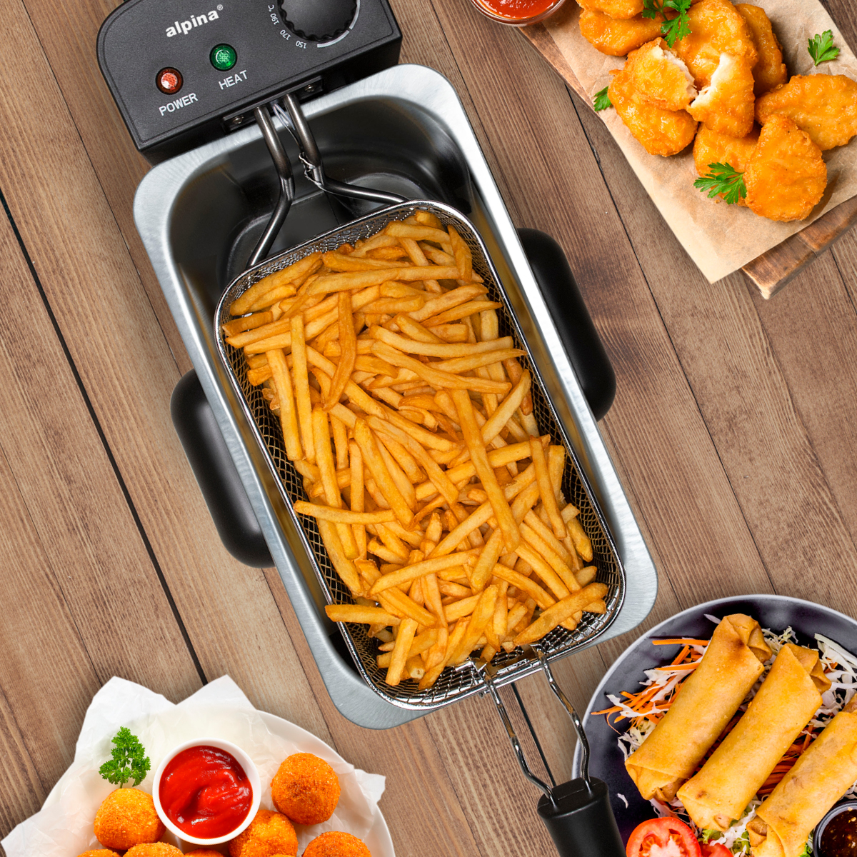 Van bovenaf gezien een friteuse met friet. Nuggets en loempia's aan de zijkant, met ketchup en peterselie.