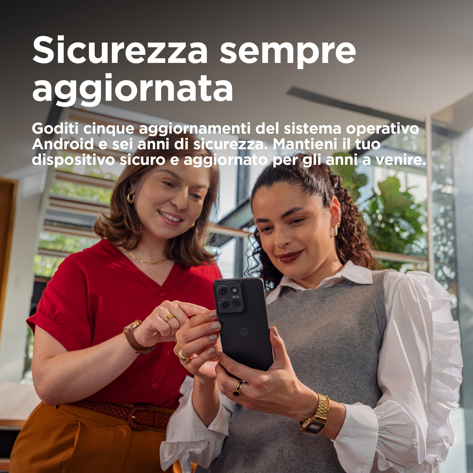 Dwie kobiety patrzą na telefon. Jedna go trzyma. Telefon jest czarny. Nowoczesne wnętrze w tle.