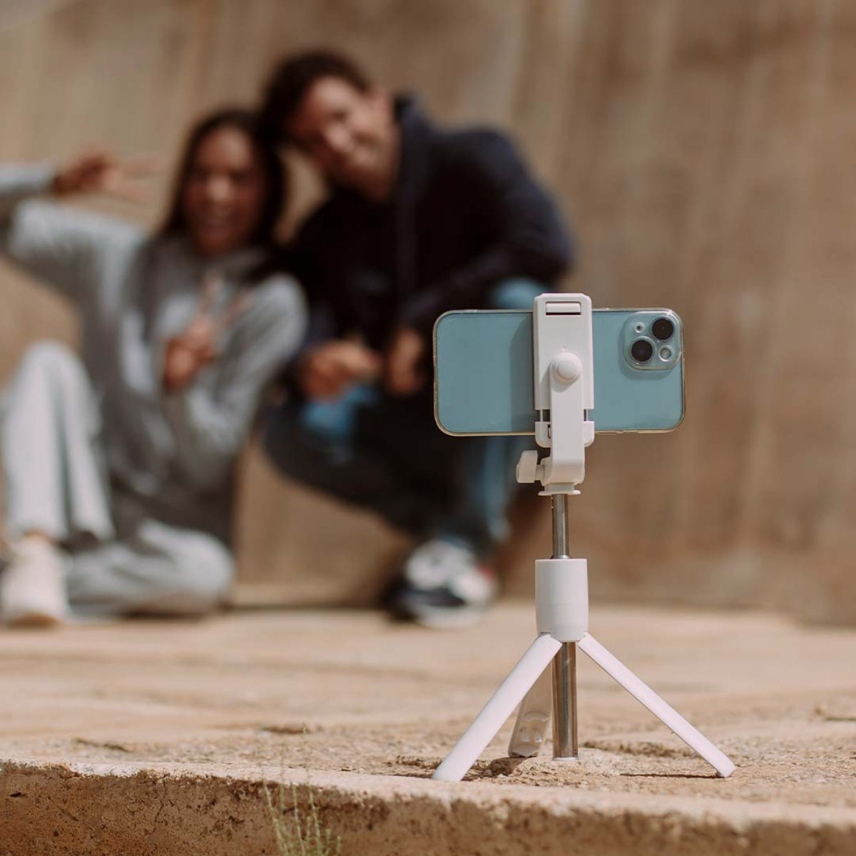 Una pareja se hace un selfie con un teléfono en un trípode al aire libre. Fondo borroso con aspecto soleado.