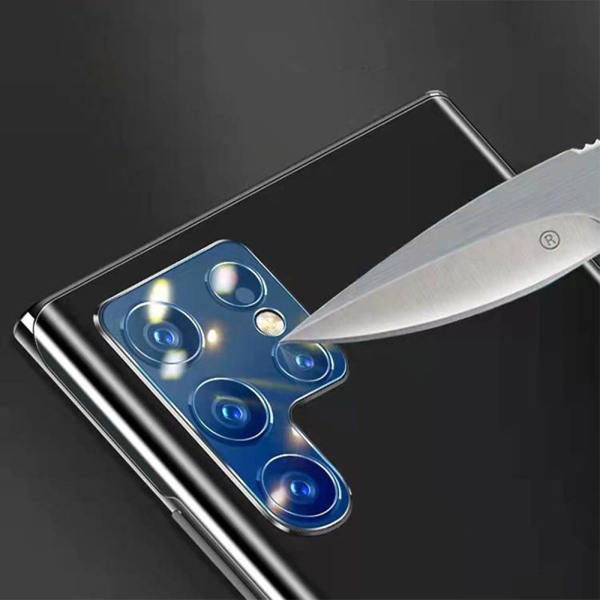Coltello che taglia una protezione per l'obiettivo della fotocamera del telefono. Il telefono è nero.