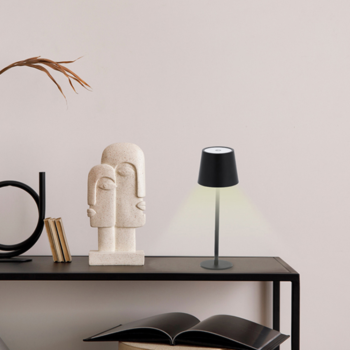 Una lámpara de mesa negra con pantalla, junto a una estatua y un libro.