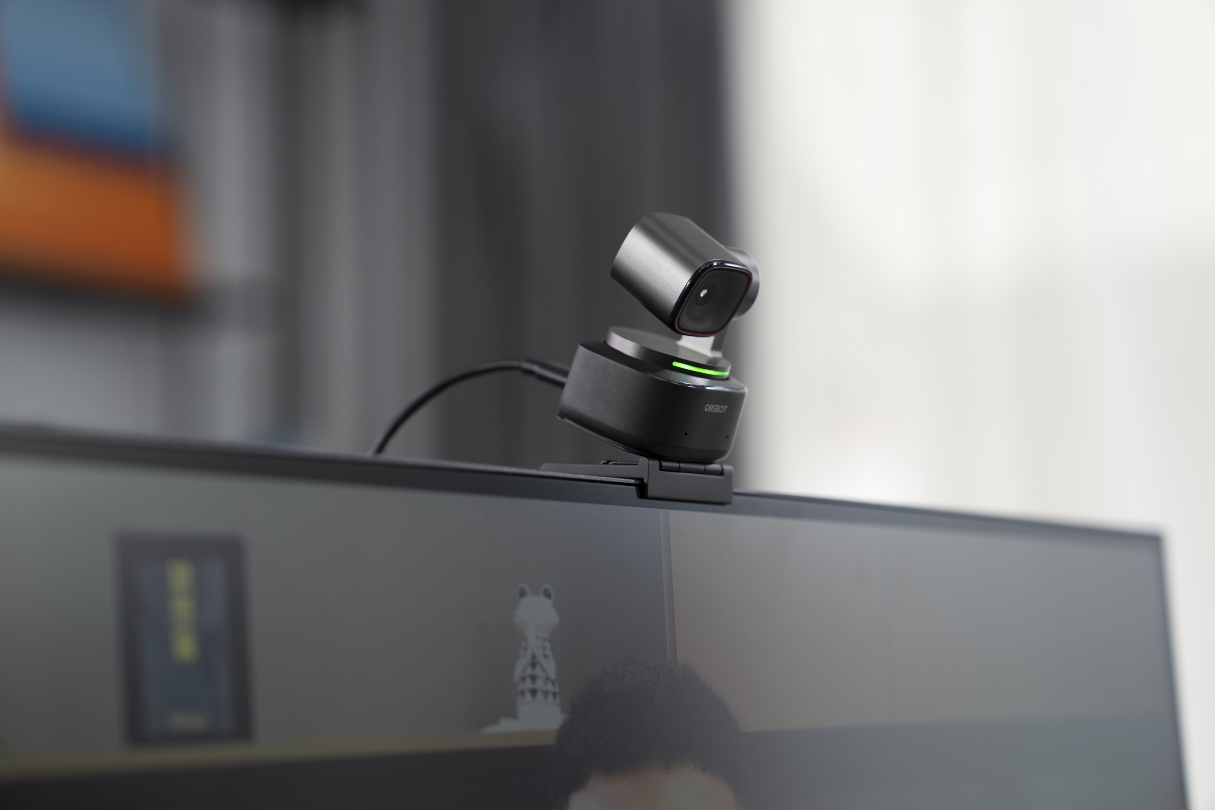 Kamera internetowa zamontowana na monitorze komputera. Czarna, ze srebrną górą. Rozmyte tło.