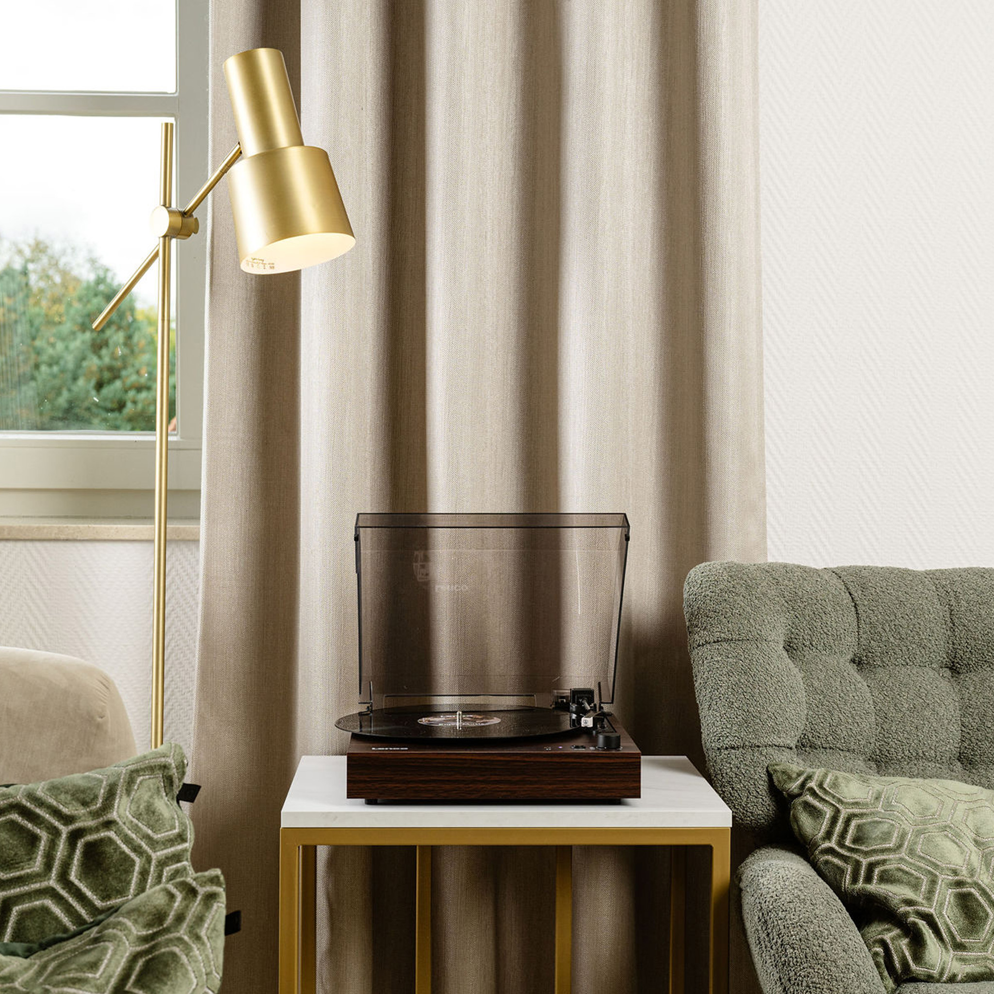 Gramofon na stole z lampą i dwoma krzesłami w pokoju z zasłonami.