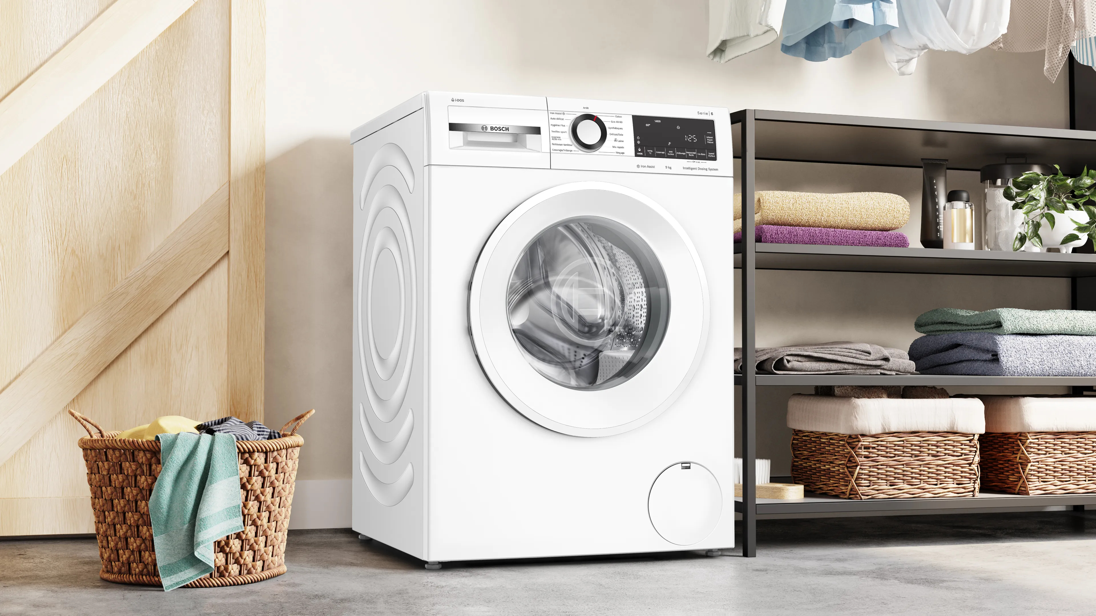 A white Bosch washing machine in a laundry room. There's a basket of clothes and shelves.