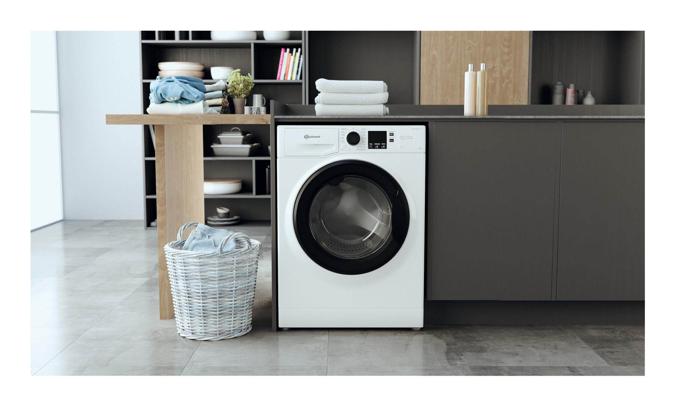 Weiße Waschmaschine in moderner Küchenumgebung. Ein Korb mit Kleidung und ein Holztisch sind vorhanden.