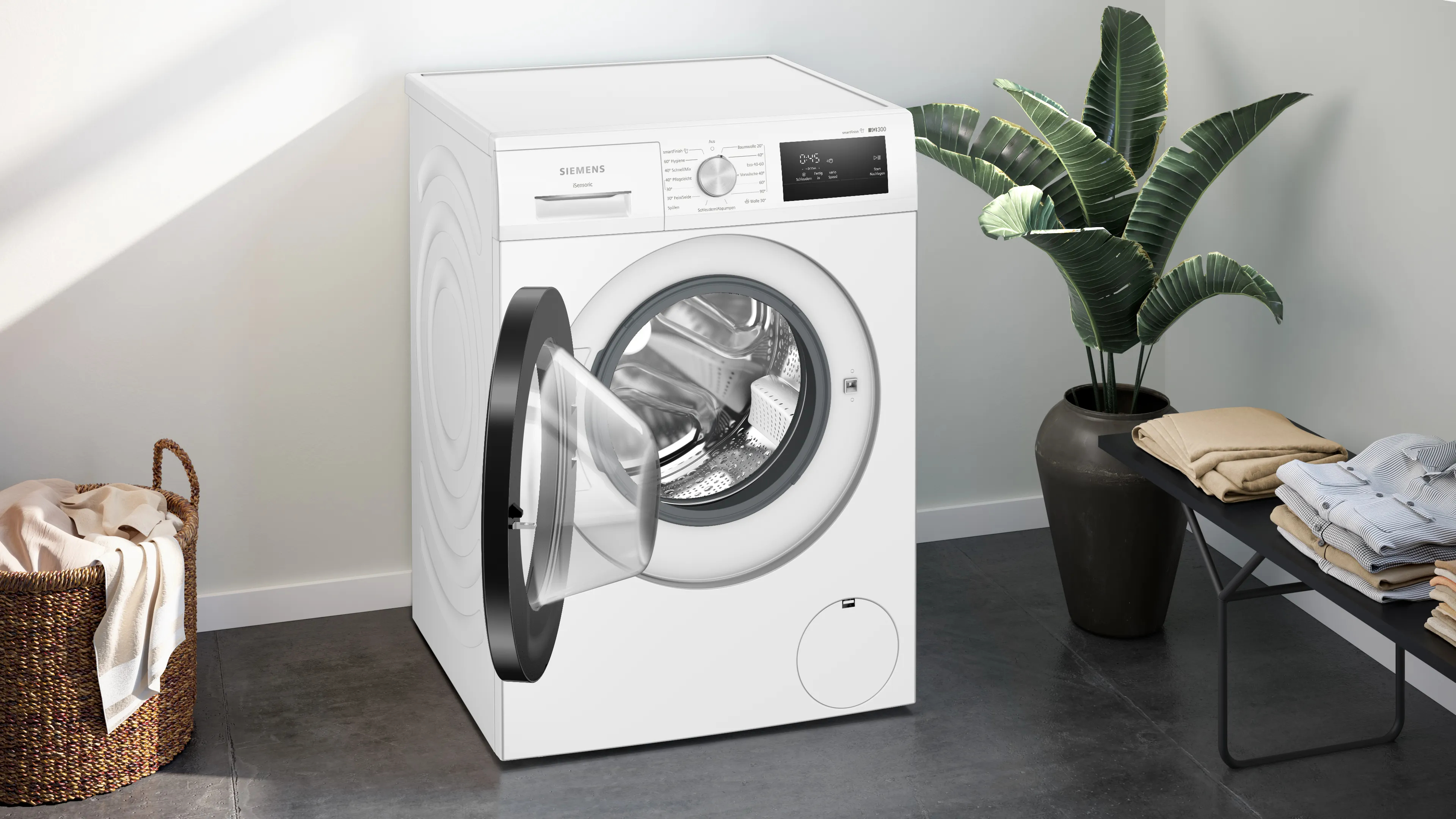 Weiße Siemens Waschmaschine mit offener Tür, neben Pflanze und Wäschekorb.
