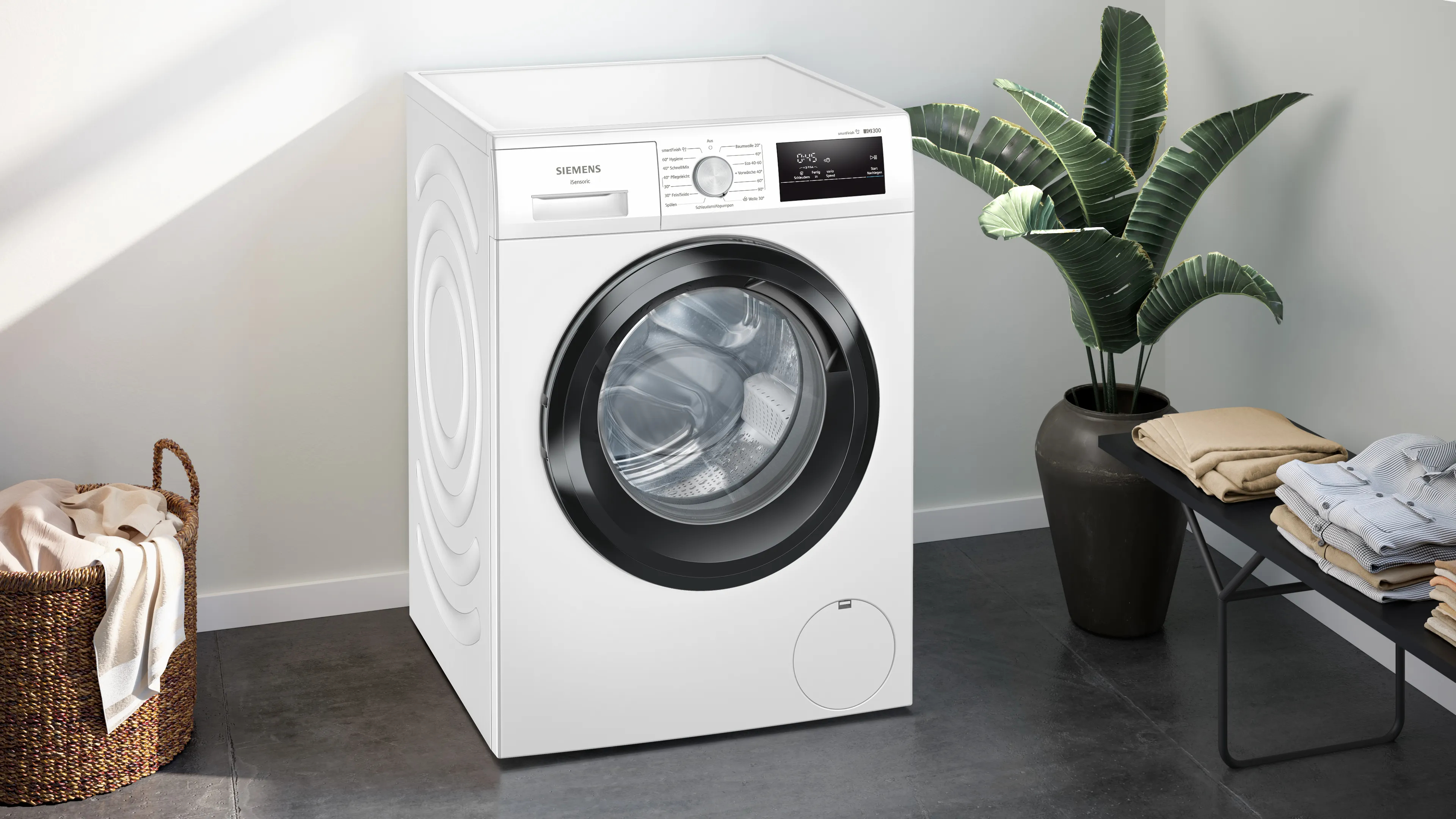 Weiße Siemens Waschmaschine. Eine Pflanze im Topf im Hintergrund, Wäschekorb links.