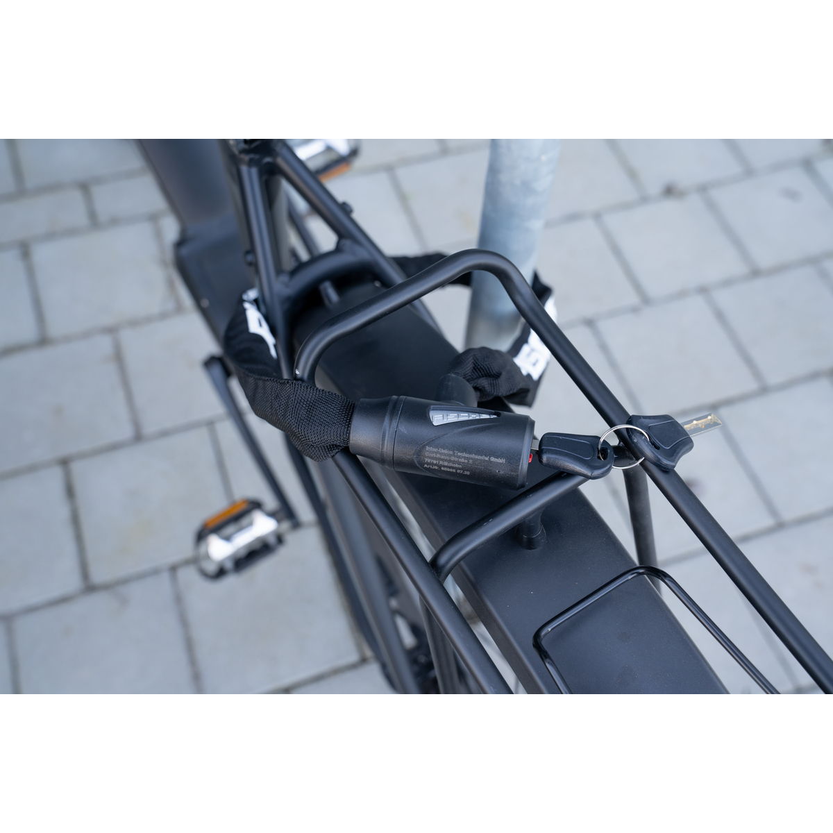 Schwarzes Fahrrad mit Kettenschloss an einem Pfosten befestigt. Schlüssel im Schloss.