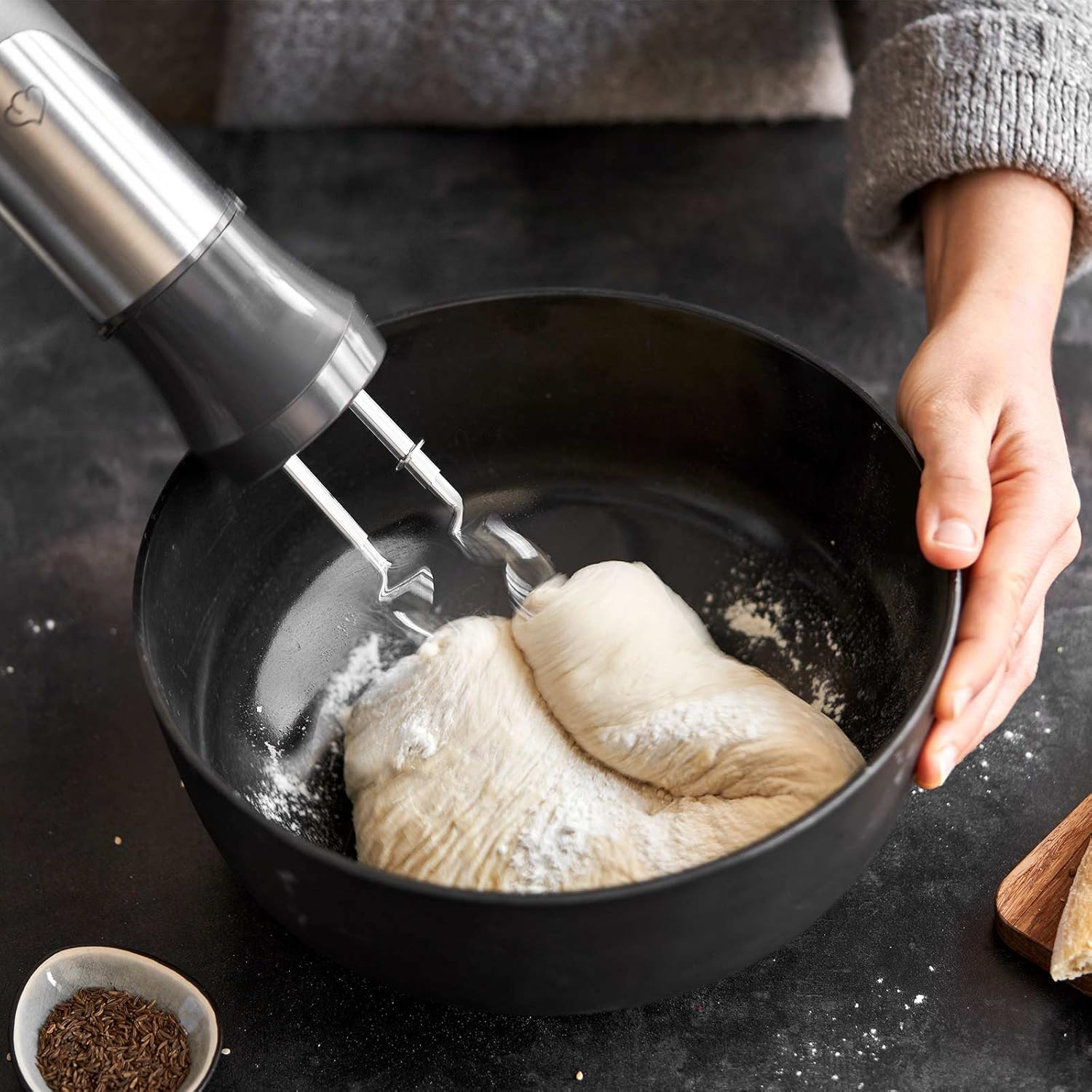 Person verrührt Teig in einer schwarzen Schüssel mit einem Handmixer. Zutaten drumherum.