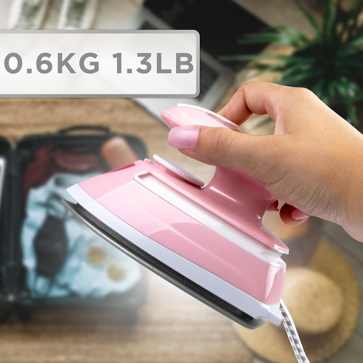 Ein rosa-weißes Reisebügeleisen, gehalten von einer Hand, mit einem Gewichtsetikett darüber.