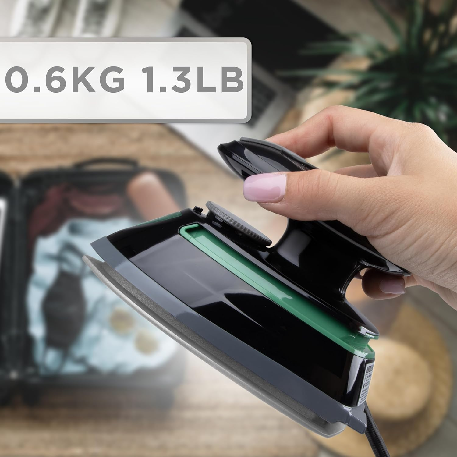 Ein schwarzes Bügeleisen auf einem Holztisch, gehalten von einer Hand. Der Text lautet 0,6KG 1,3LB.