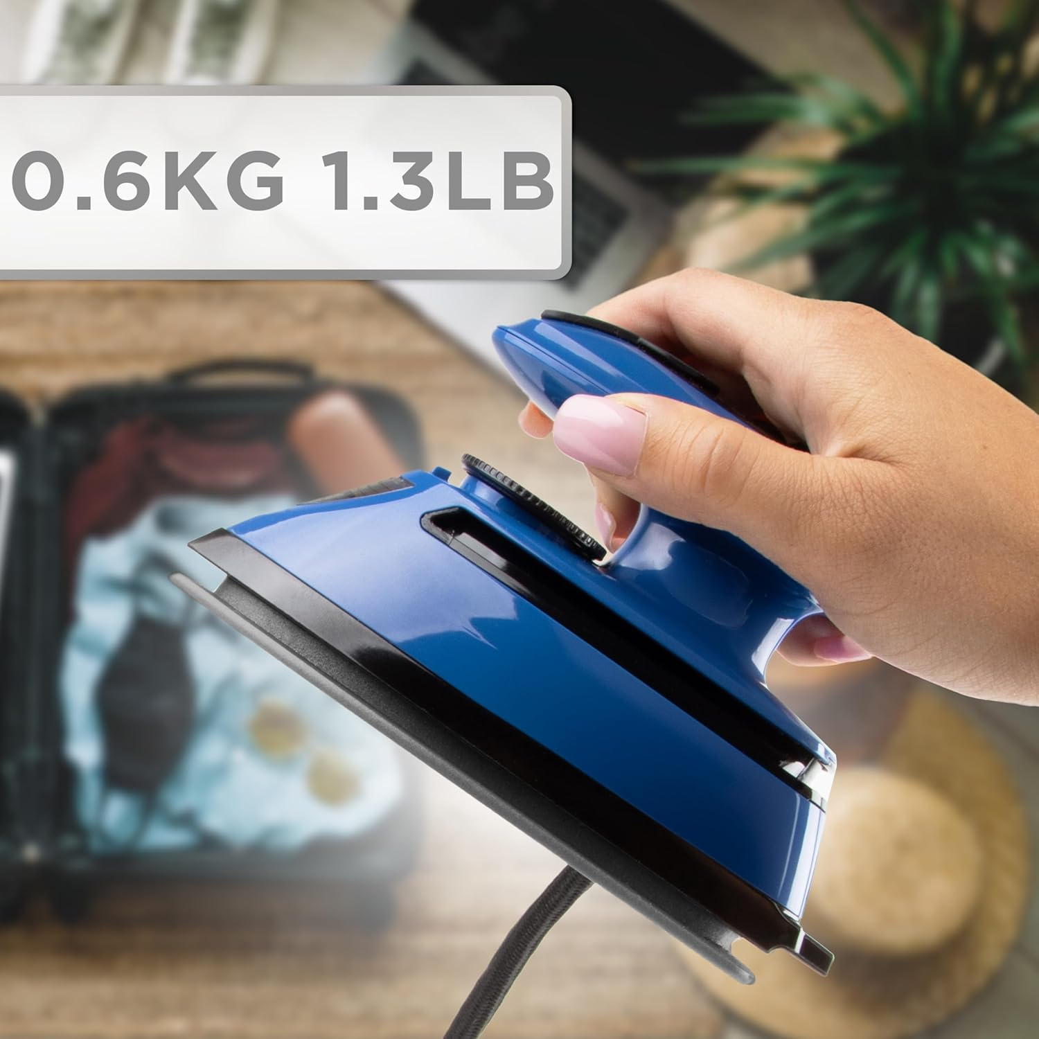 Eine Hand hält ein blaues Handbügeleisen, mit einer Gewichtsanzeige von 0,6 kg/1,3 lb. Hintergrund unscharf.